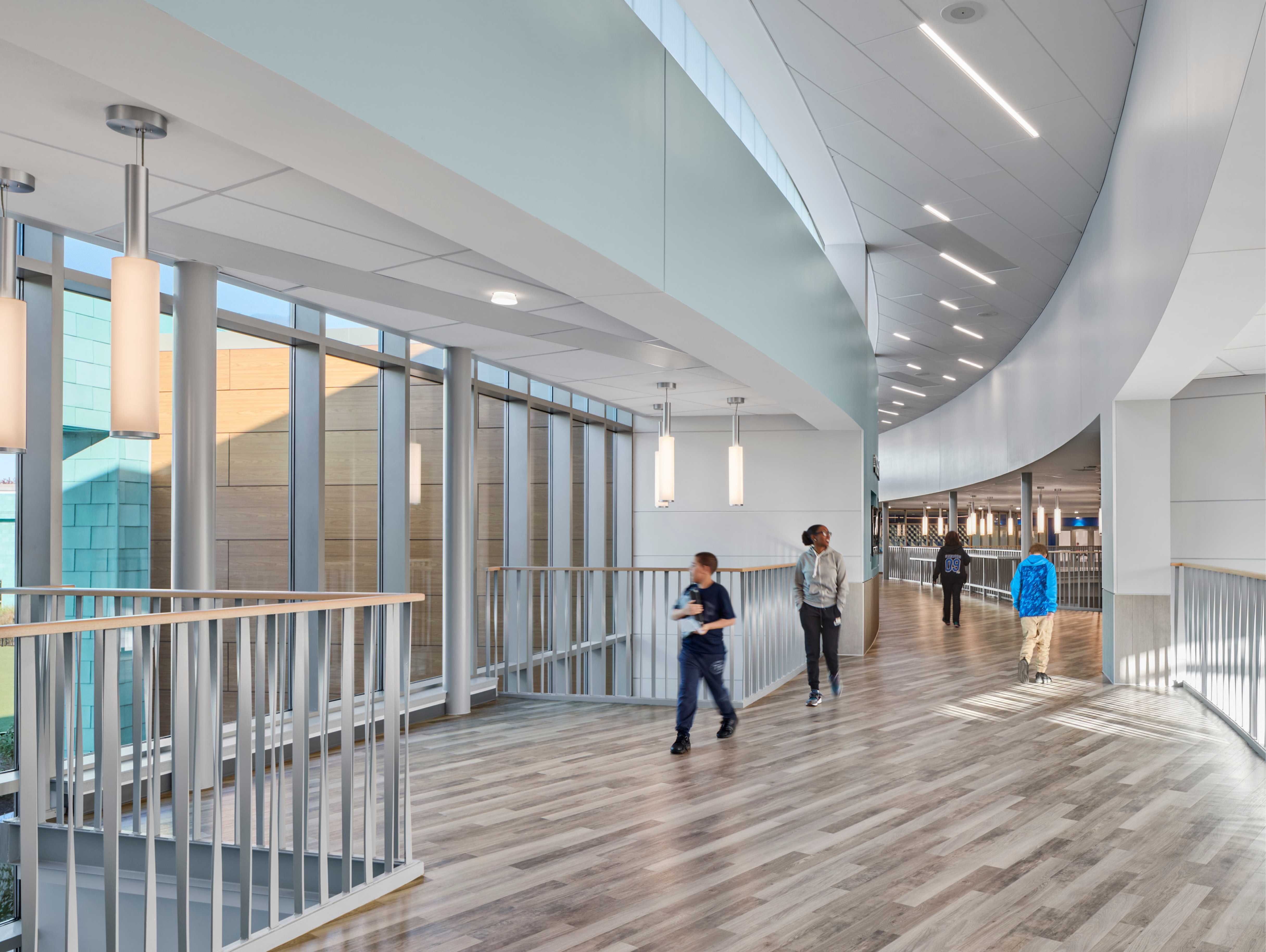 Students walking on second floor with wood floors with large windows to the left showing exterior 