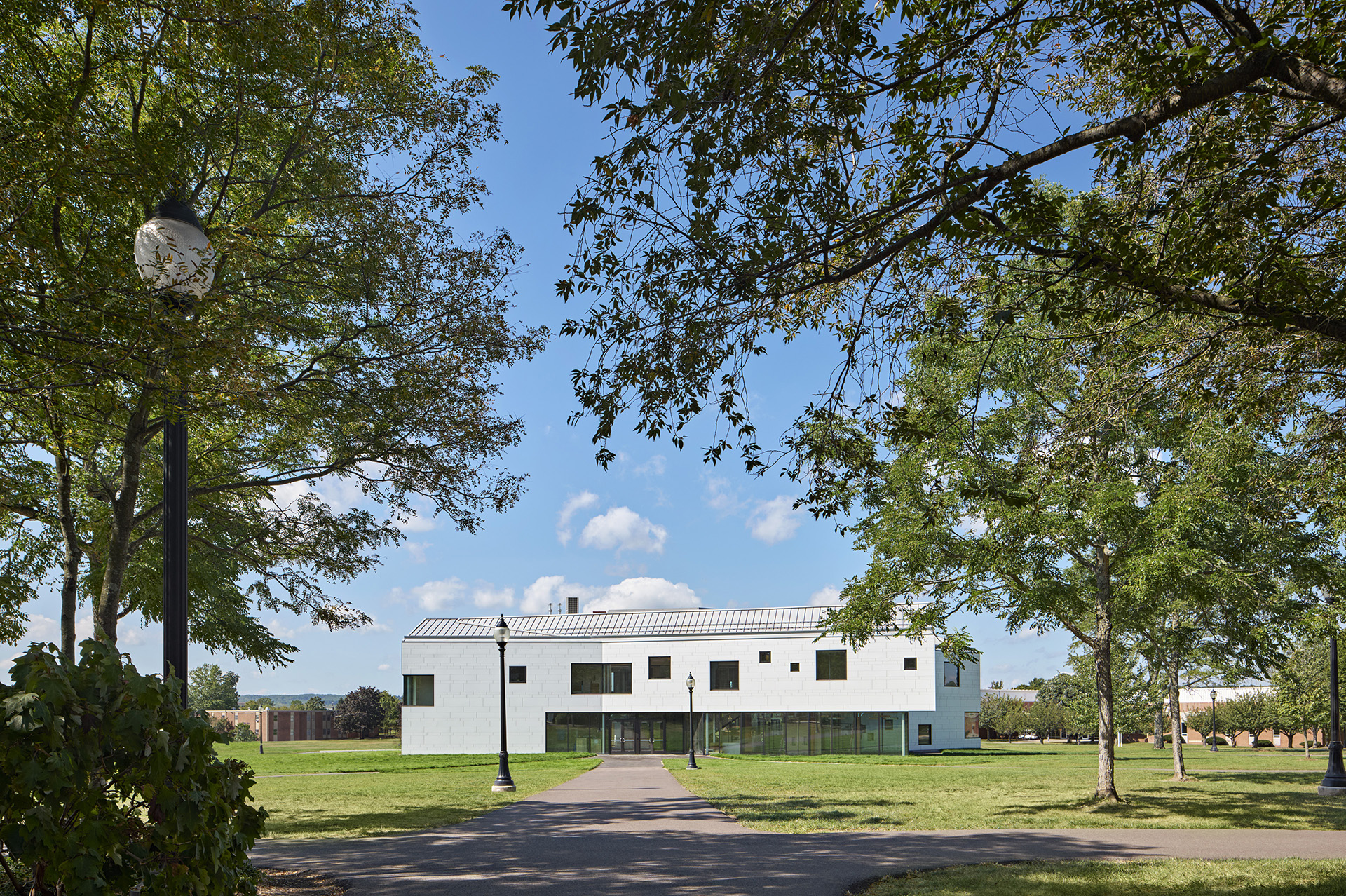 Exterior view of school with trees peering in from both sides, blue sky with clouds in background