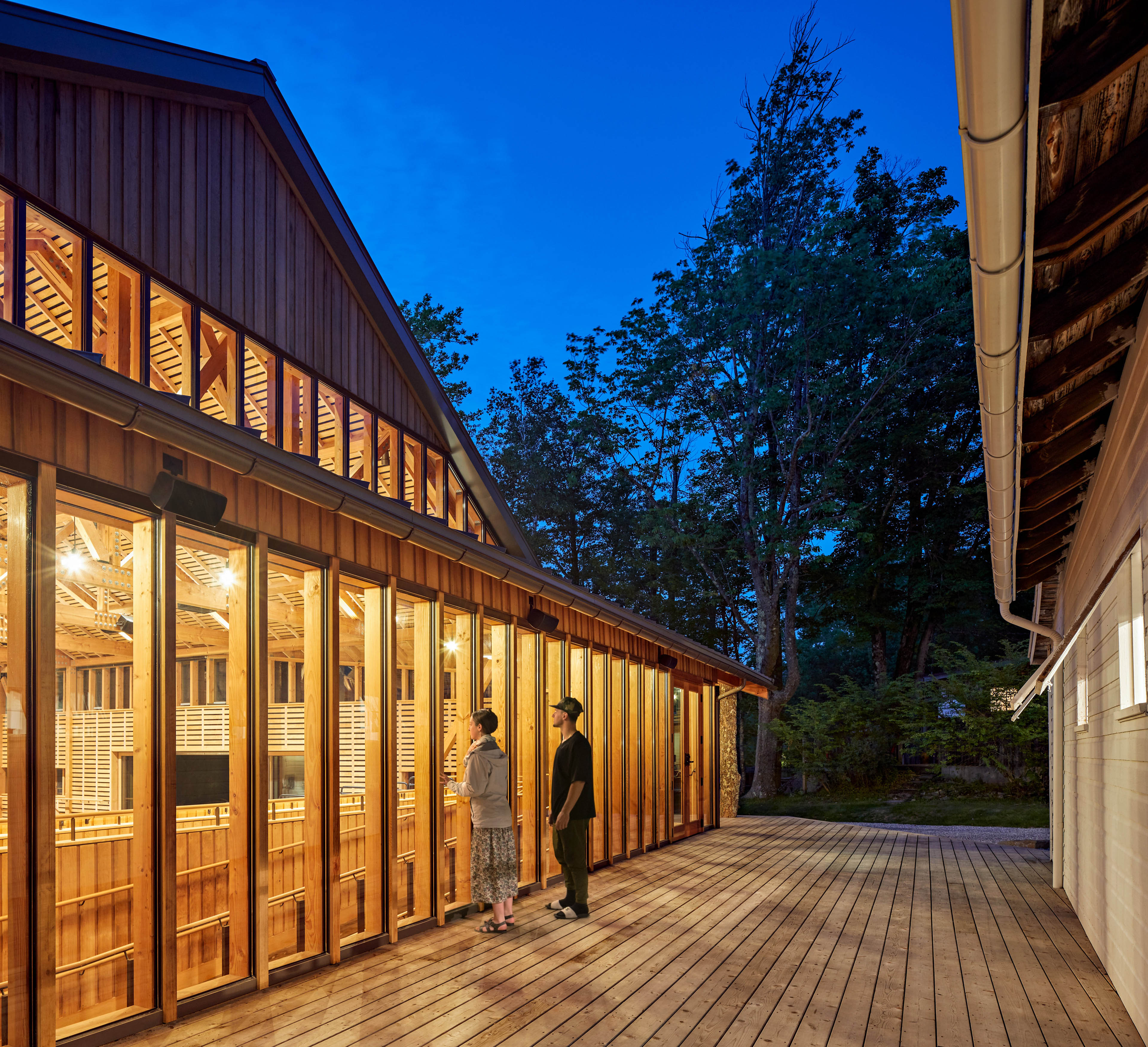 Nighttime view of patrons looking into windows of studio to the left with yellow light glowing