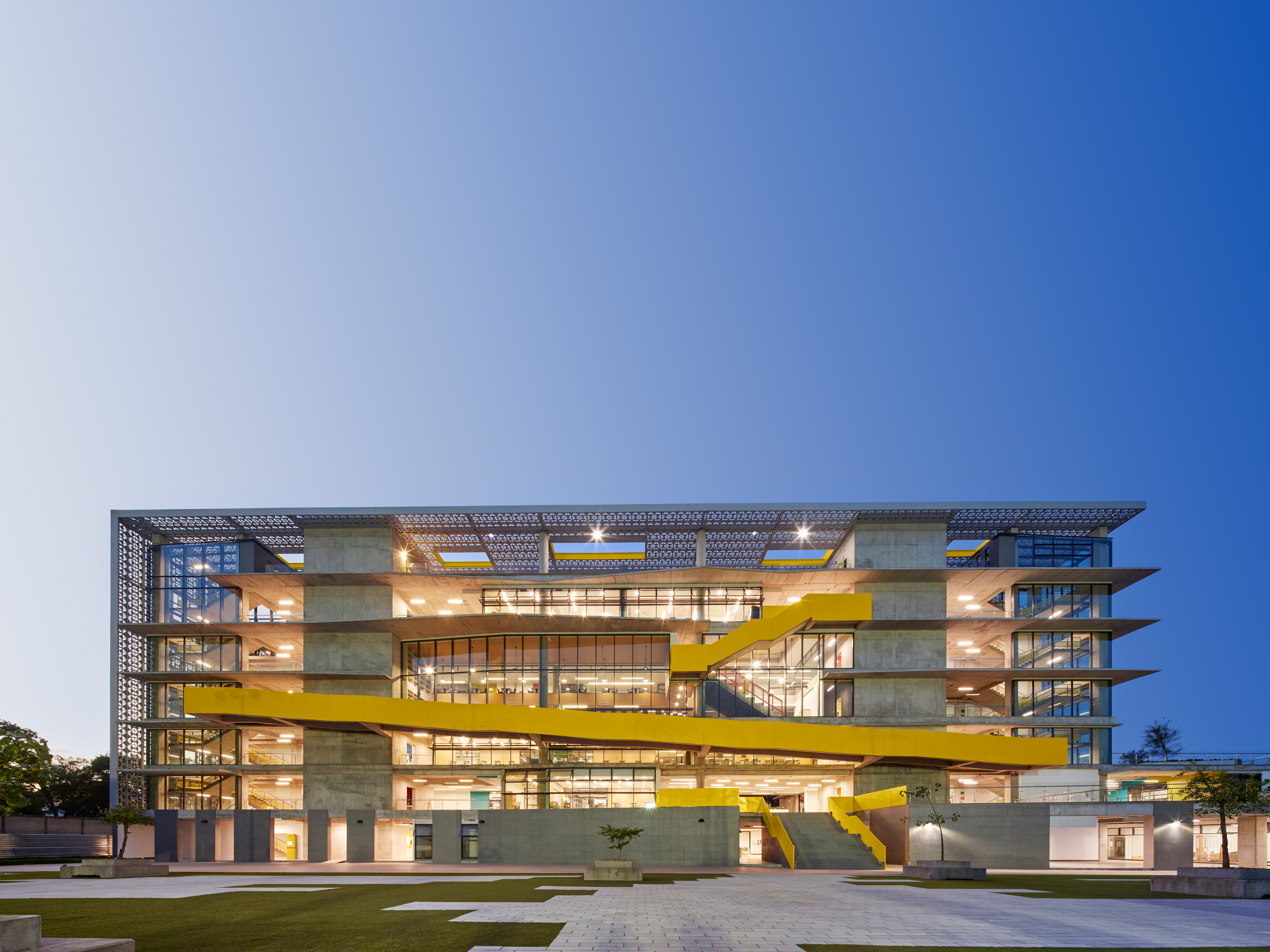 The American School Foundation of Guadalajara with seven levels, vertical windows on the left, middle, and right side with beams separating each side and yellow metal strung throughout