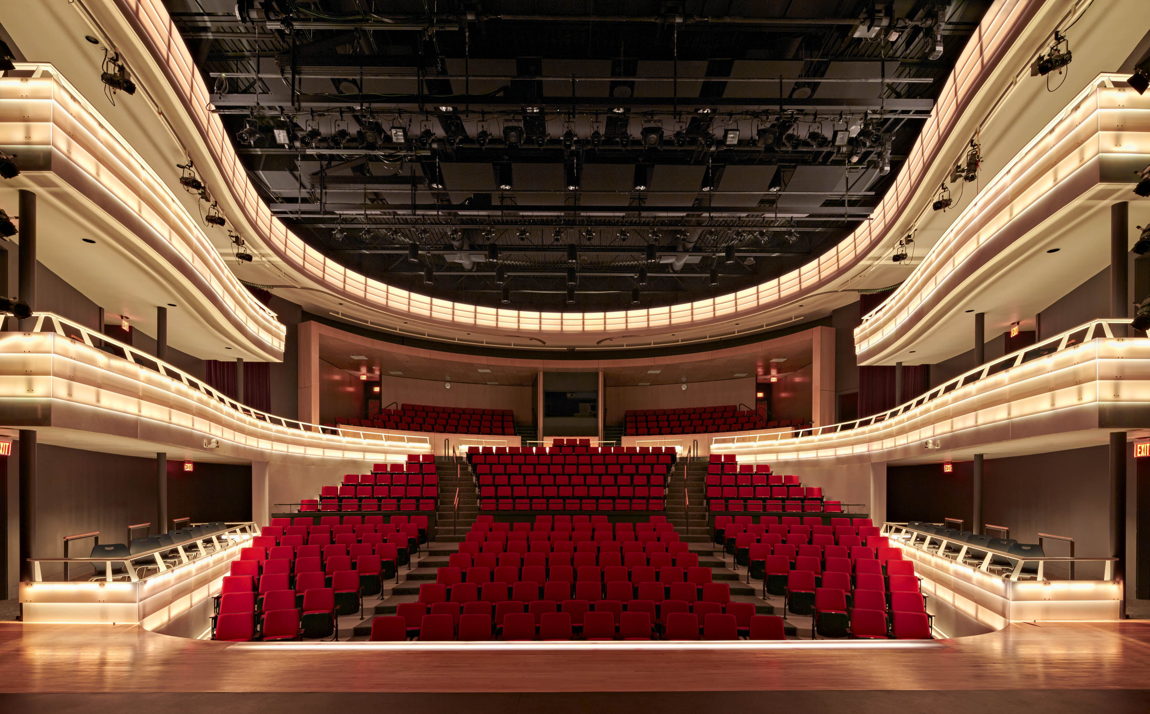 Theater with rounded seating area with red seats, 3 balconies illuminated from stage view