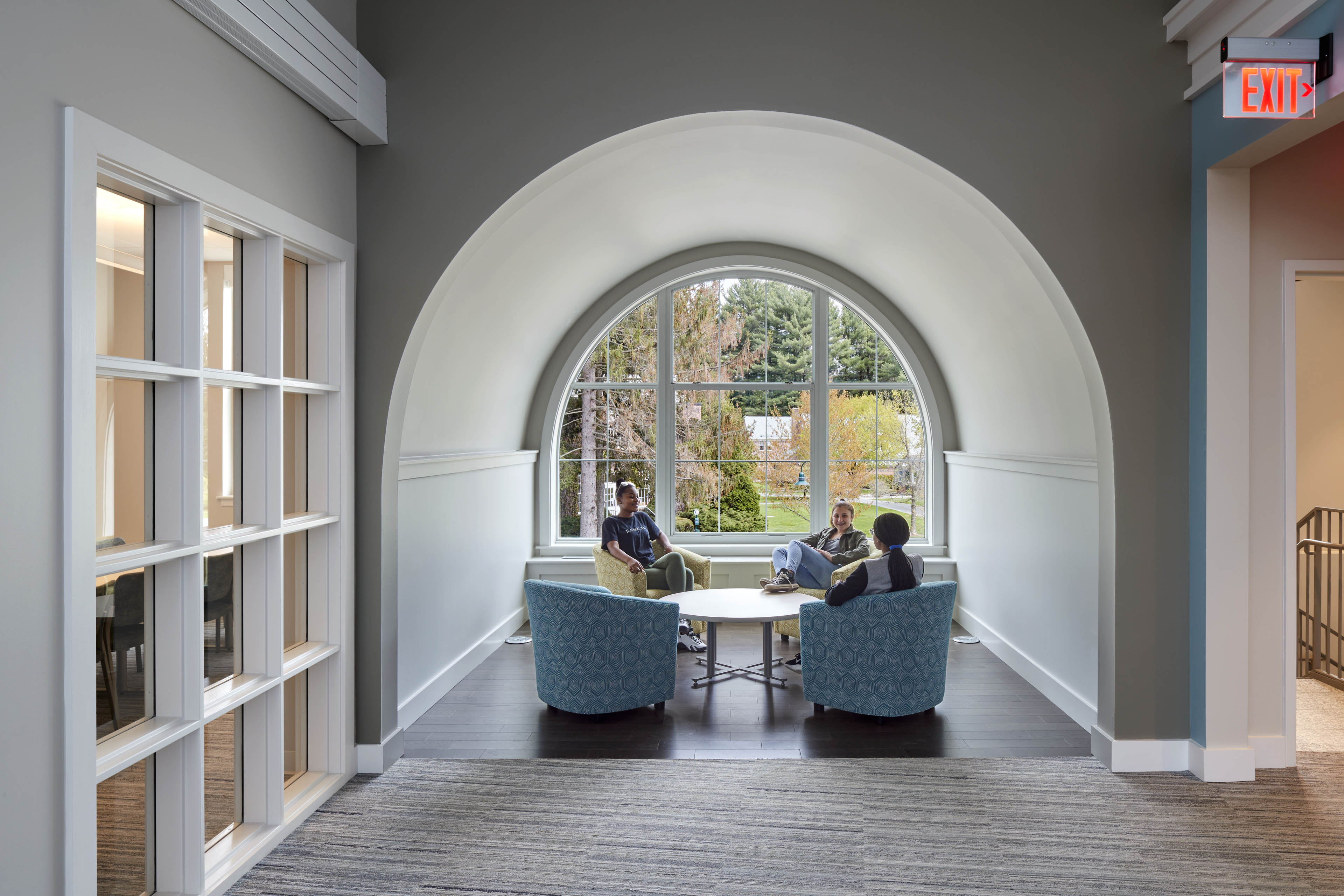 Students sat at lounge area in curved opening looking out at foliage 