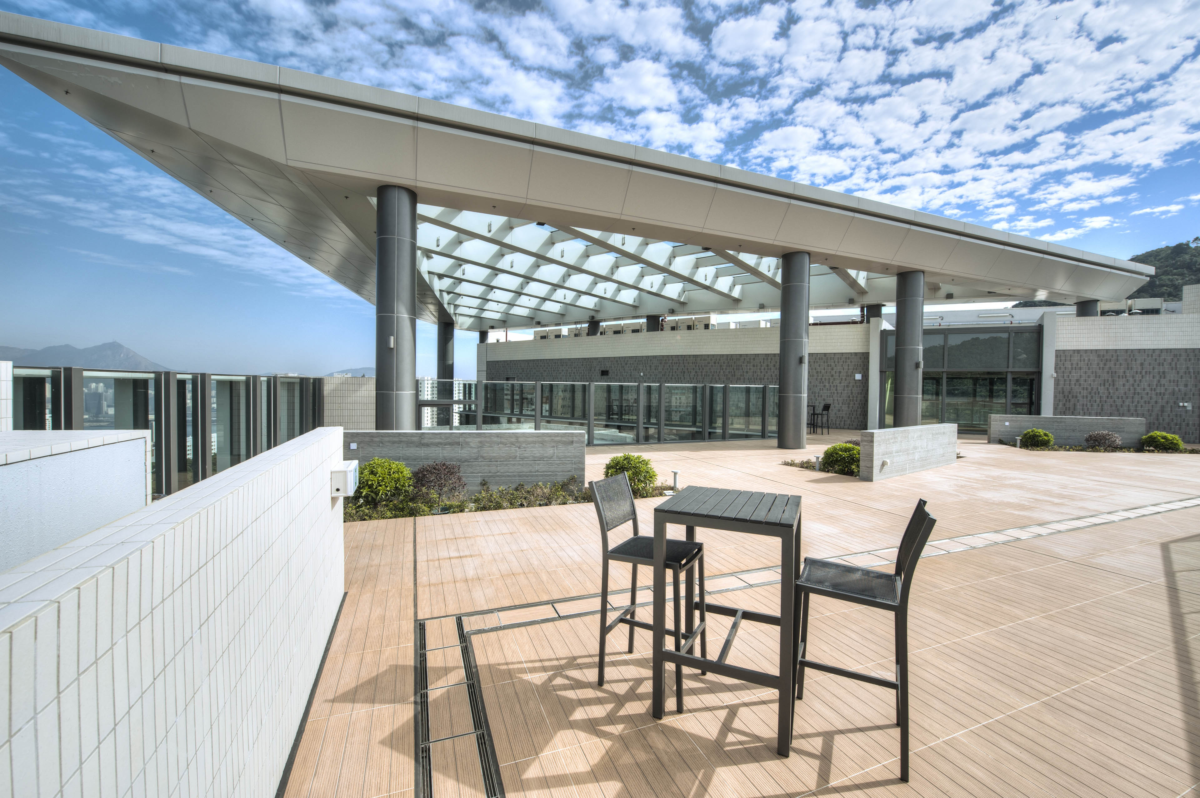 View from roof with table and chairs with large awning with geometric pattern in center. Blue sky with clouds