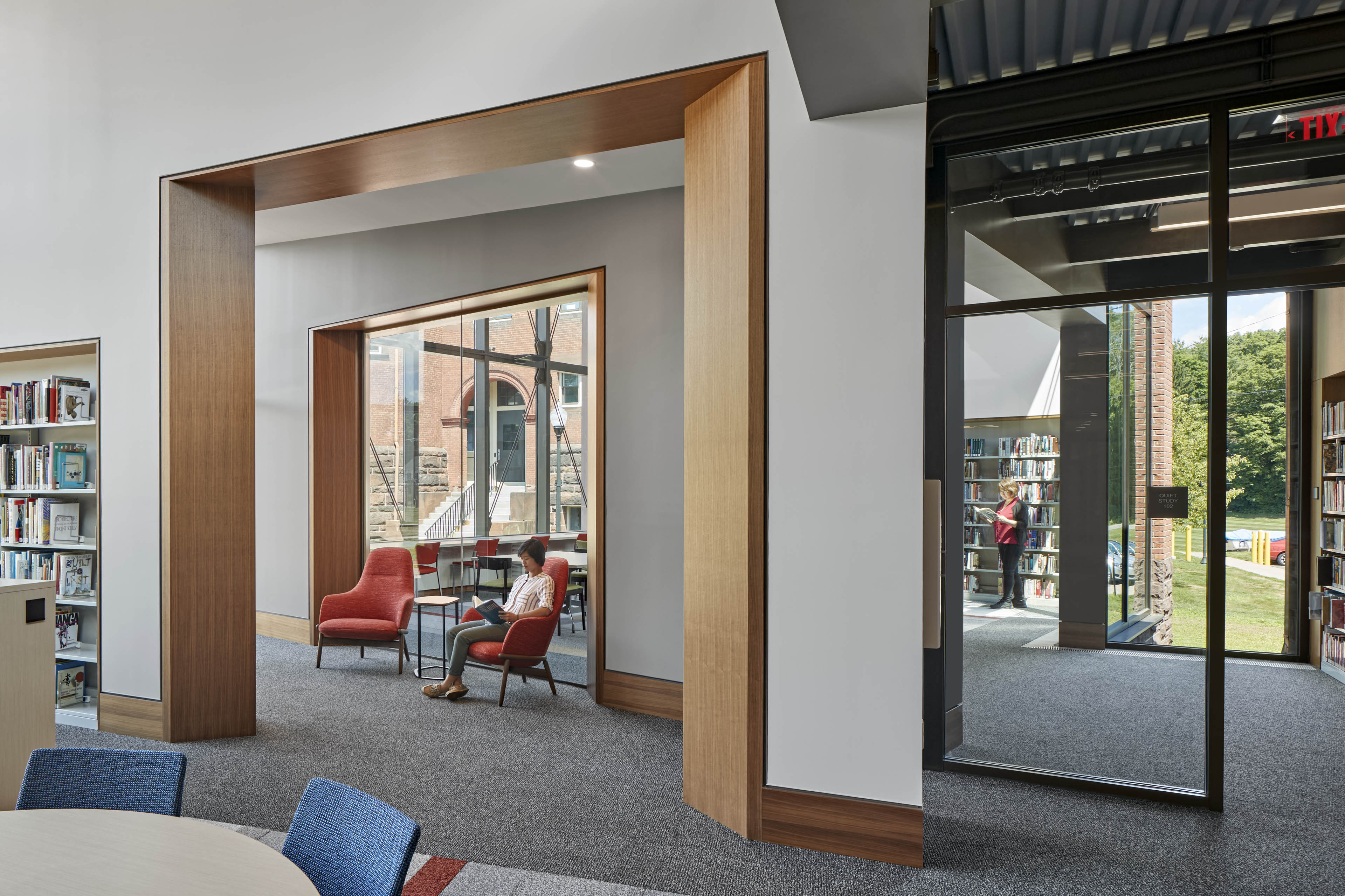 View of multiple seating areas in library with orange chairs and book shelf to the left