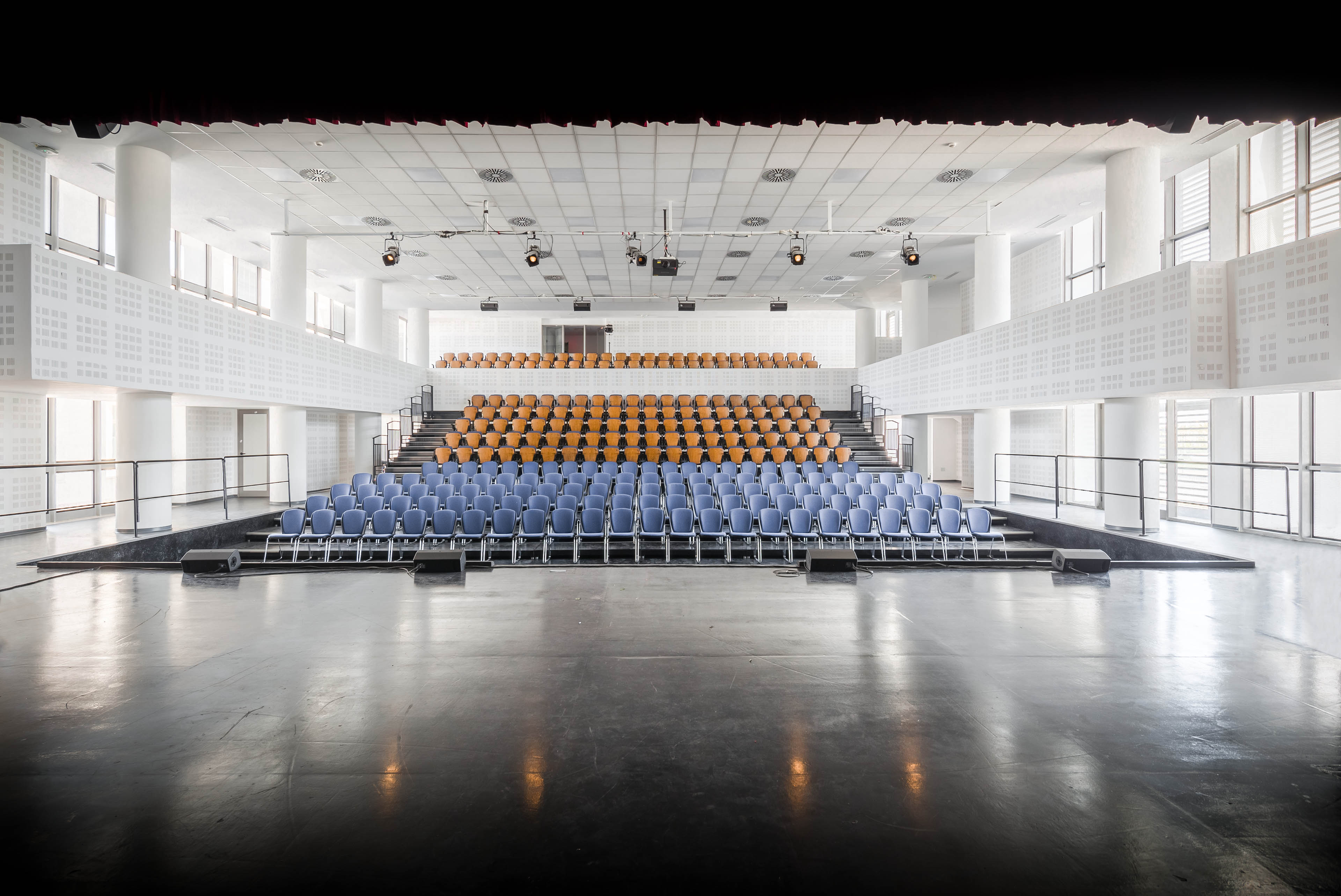 Theater with blue seats in front section and orange seats in back area, with white walls and ceiling