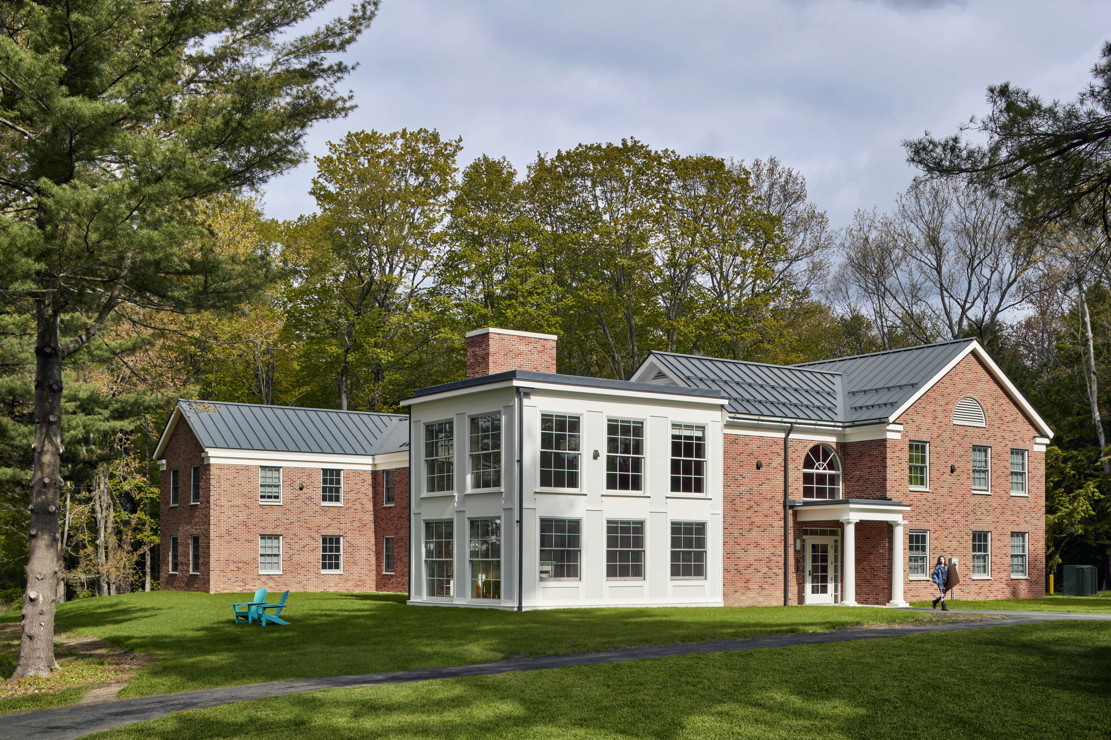 View of exterior from grass area with white building with quadrant windows sat in between brick annex's. Green grass in front with walkway through the middle