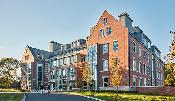 View of exterior from drop off lane, with students walking into building and sun shining 