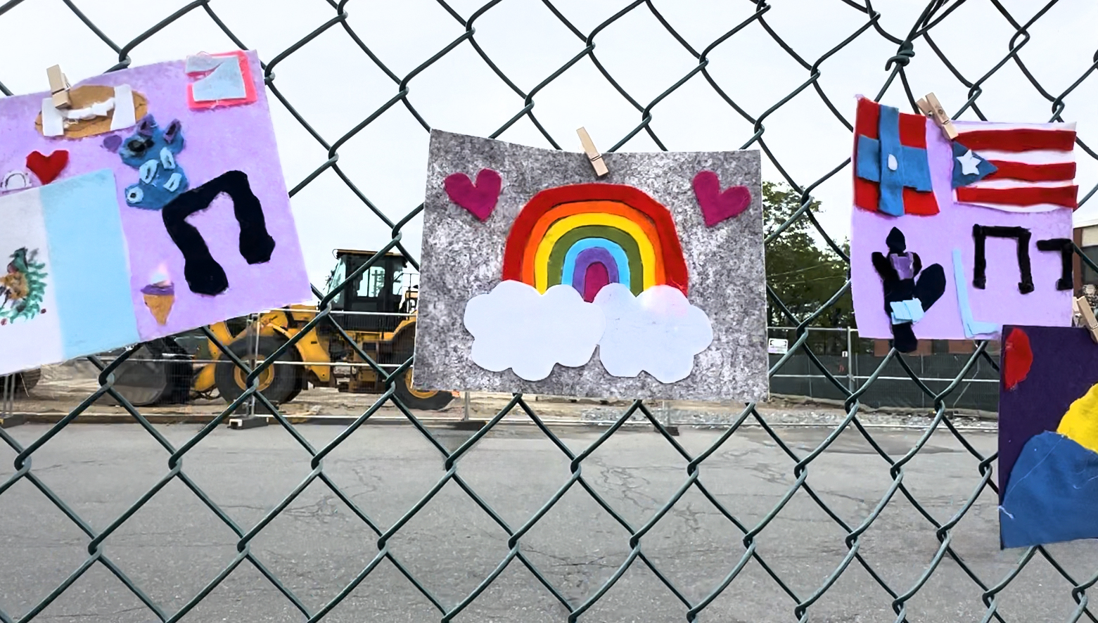 Student artwork hangs on the fence at the Esperanza Beam Signing ceremony, artwork features a rainbow on clouds with hearts surrounding