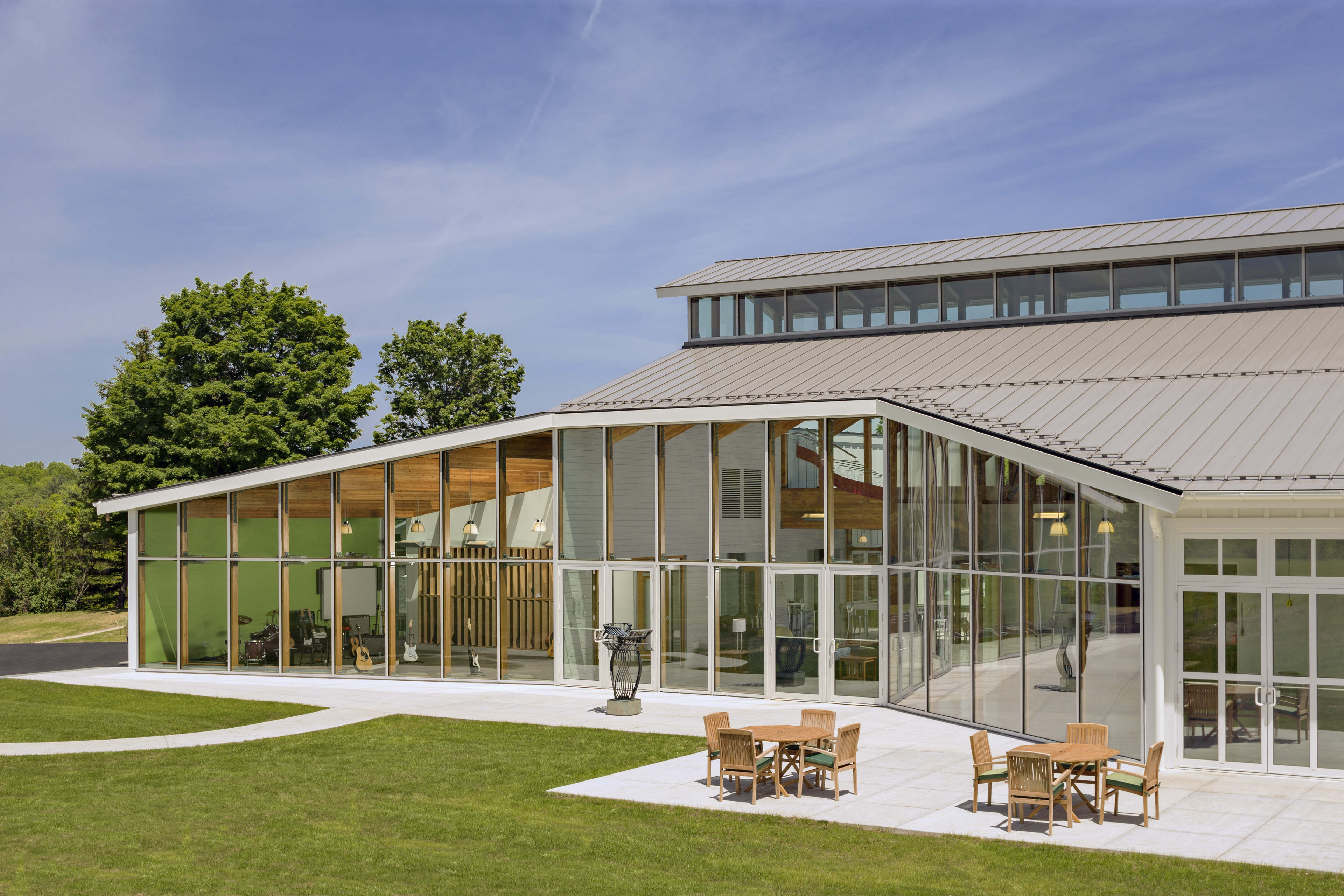 View from courtyard looking at building with floor to ceiling windows and a seating area on the front along the grass 
