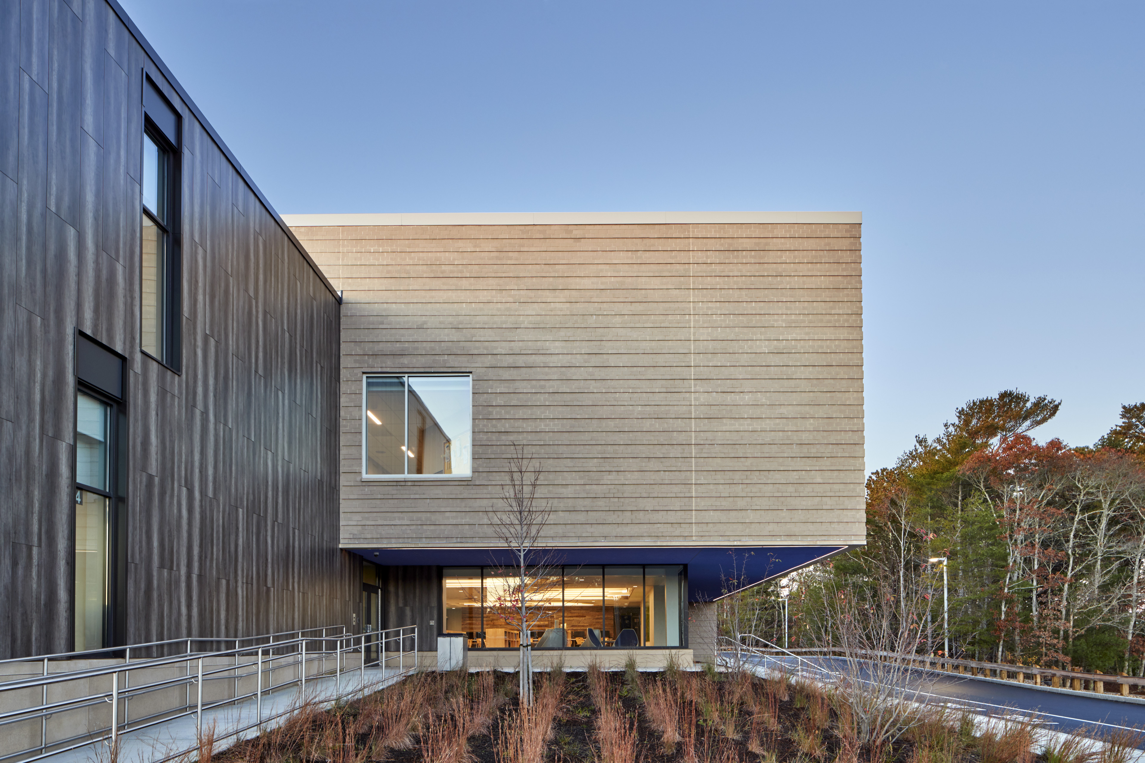 landscaping and beige wood paneling, and dark wood to the left, blue sky behind and green/auburn trees to the right
