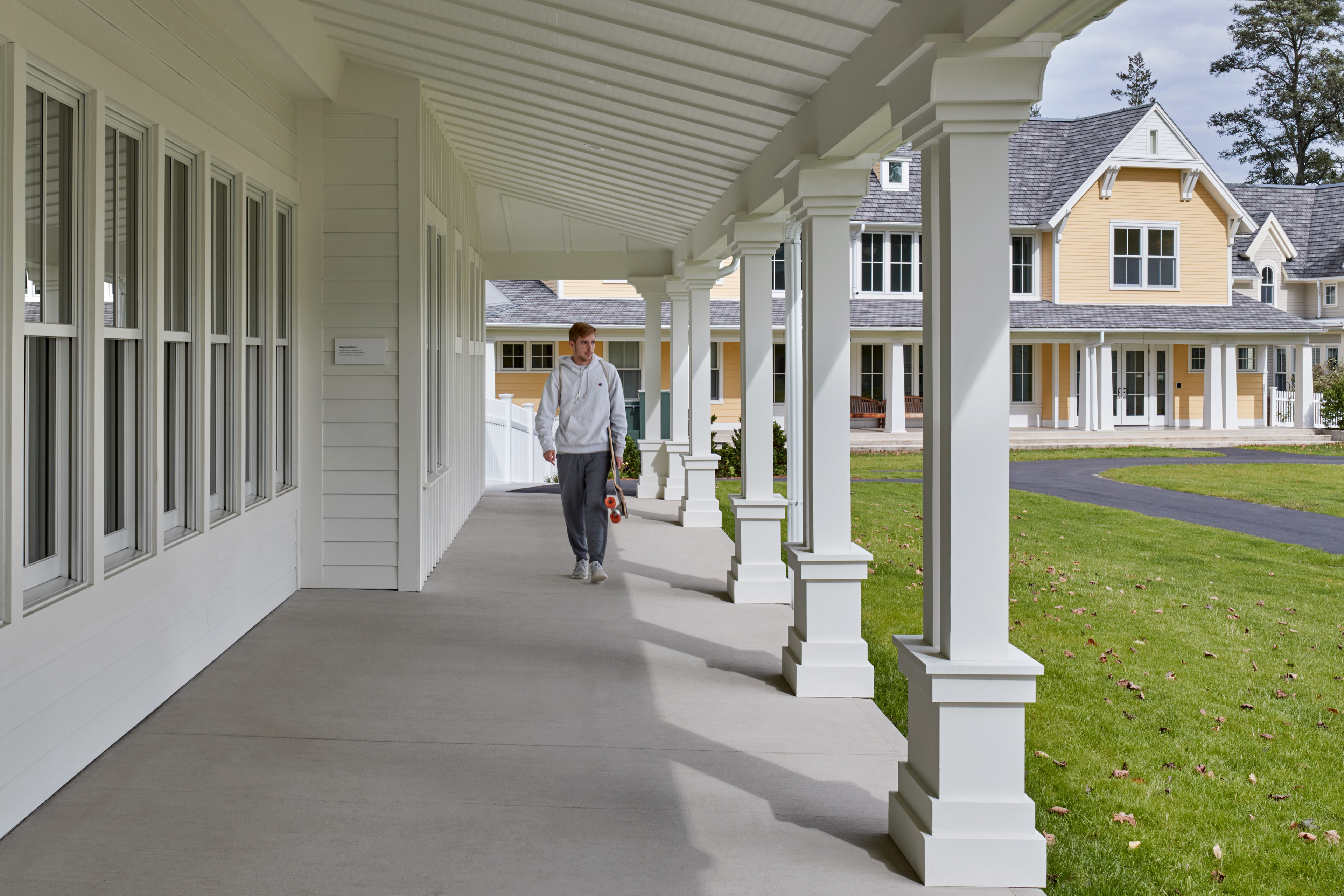 Student walking down exterior corridor with covered awning with grass and walkway to the right