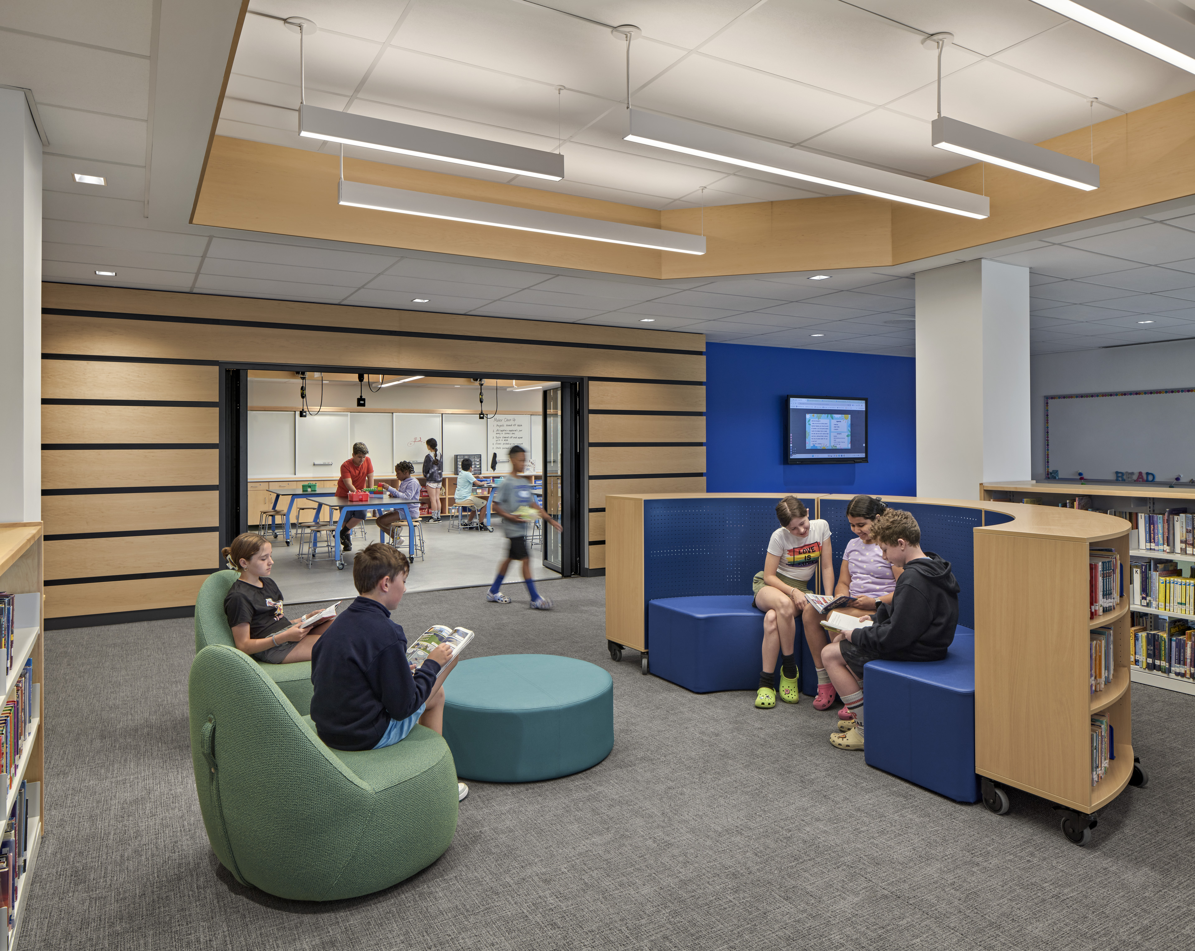 Students reading at lounge area in library with book shelves to the right and blue accent wall in the back