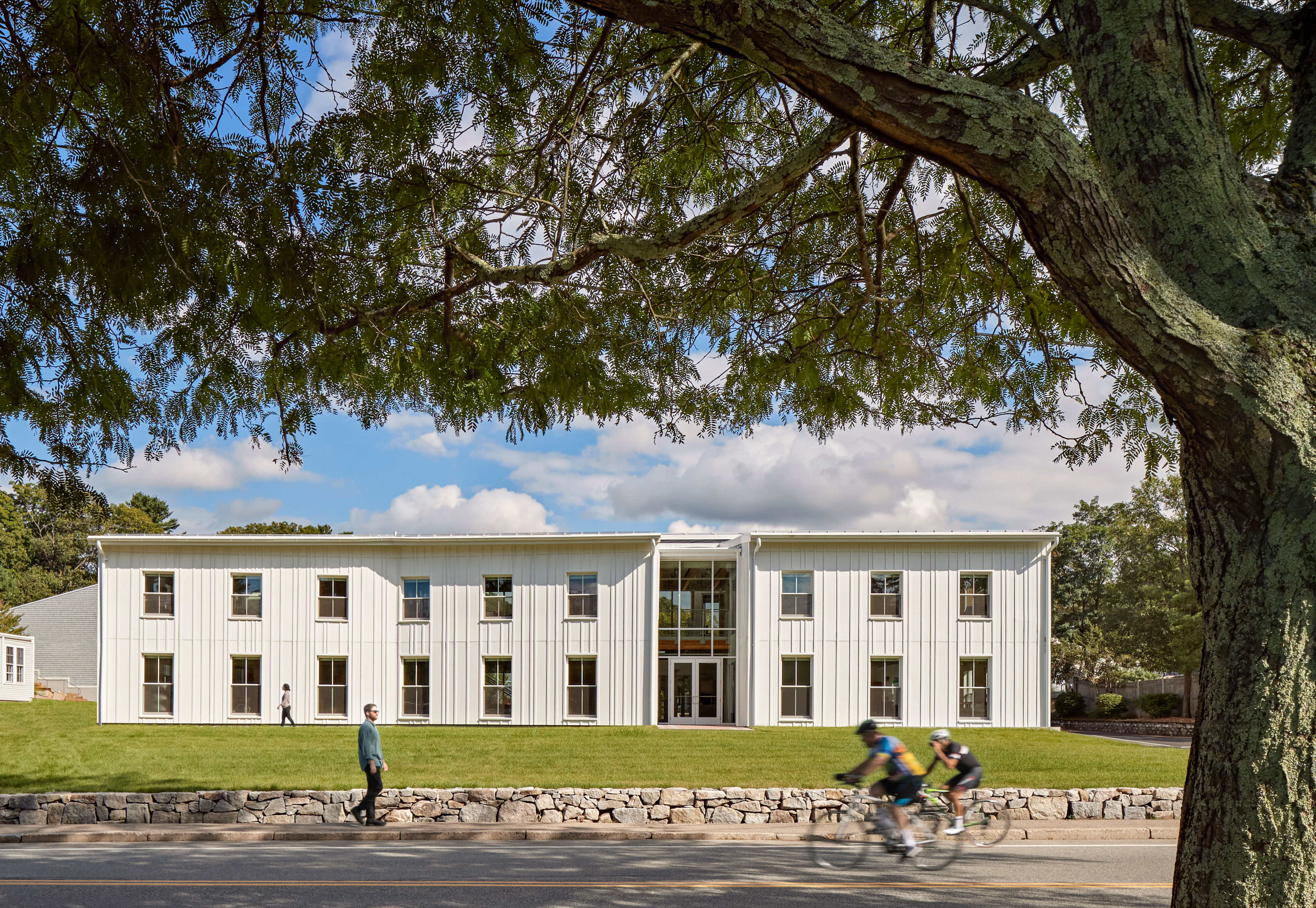 Exterior view of building with white siding and symmetrical windows and tree to the right expanding over top of photo
