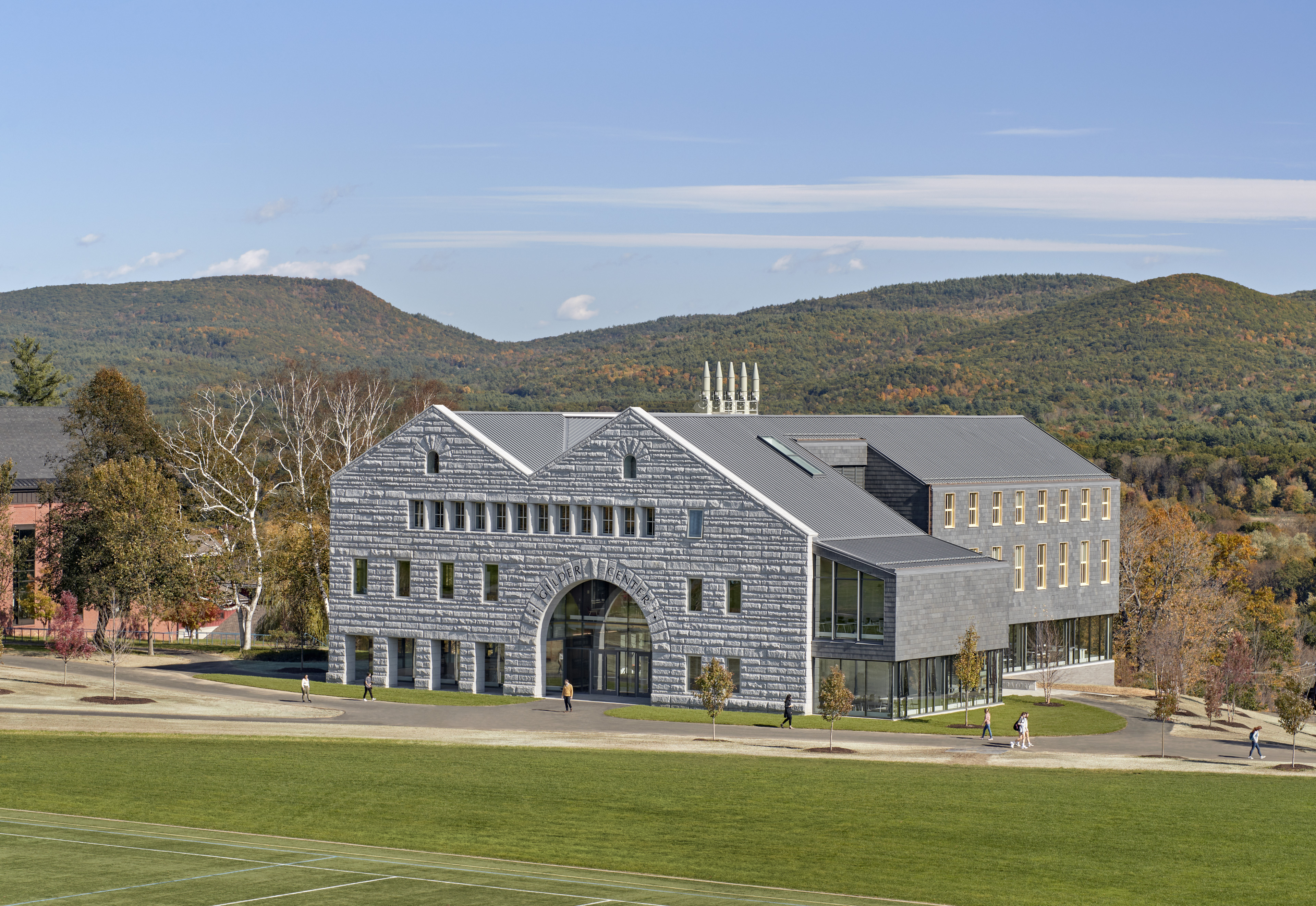 Exterior entrance with large green grass area lining walkway, autumn trees being and to the side, rolling hills with autumn trees in background