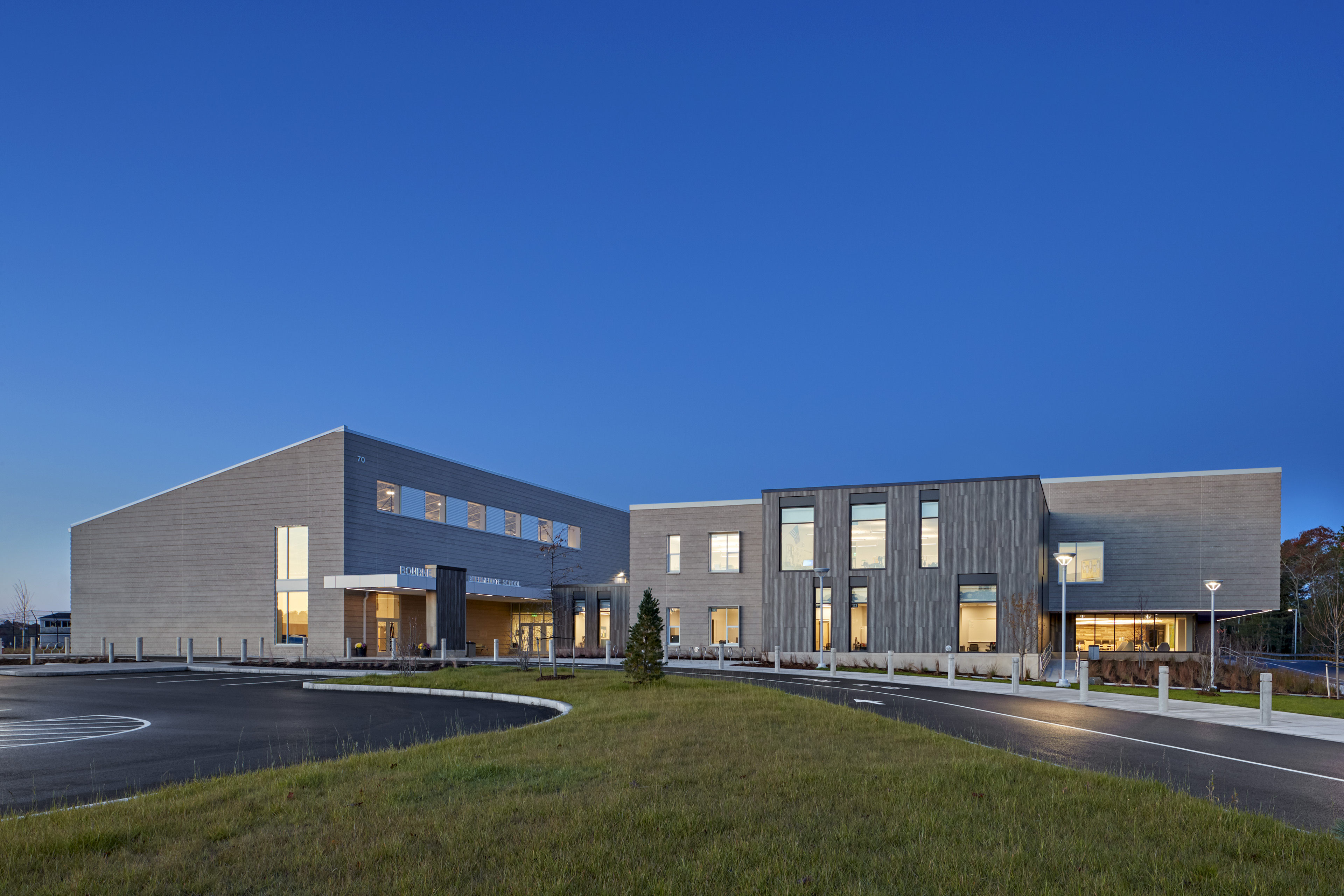 Exterior of Bourne at dusk with deep blue sky, drop off area with grass in the middle. Yellow glow from windows