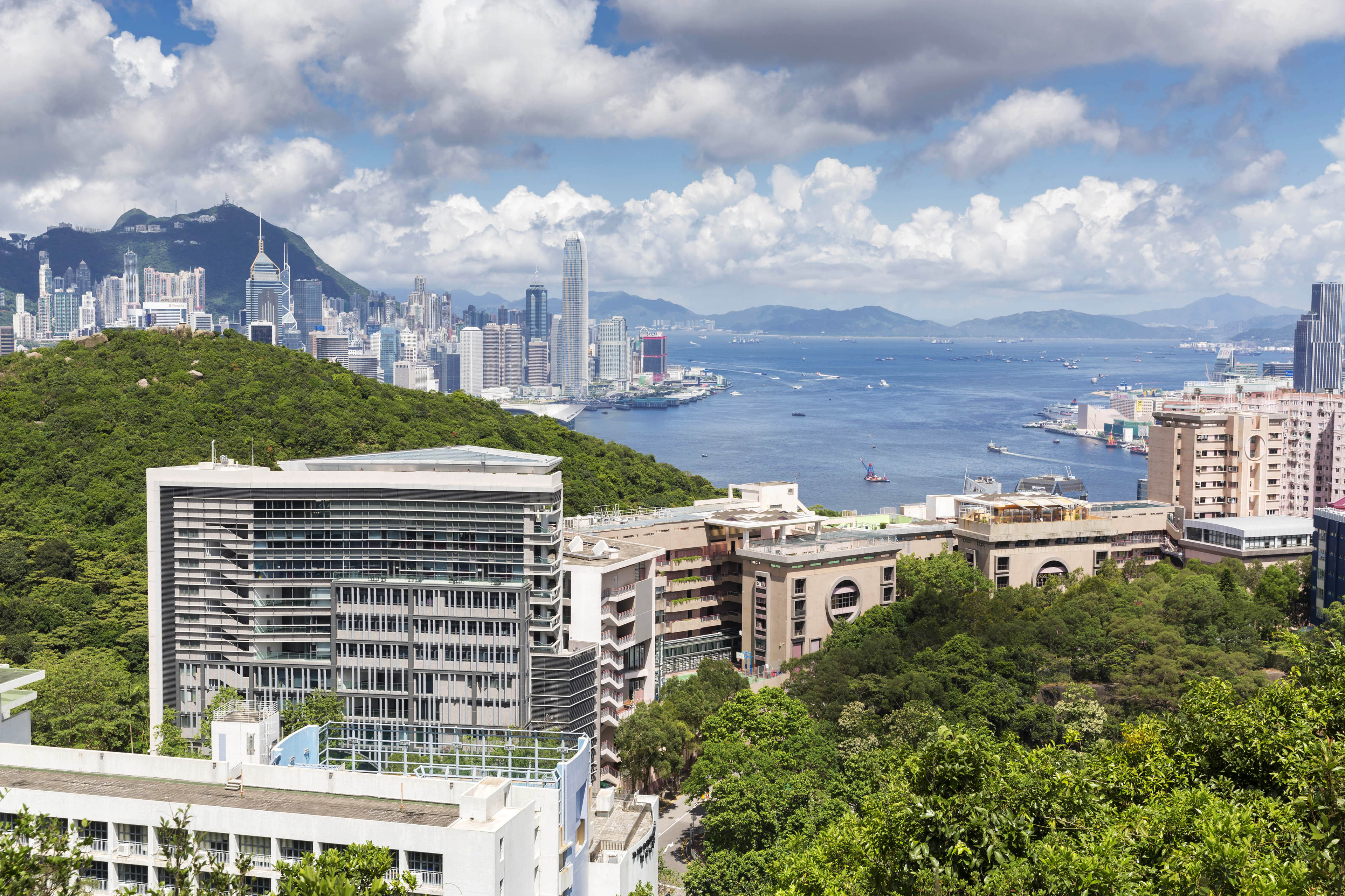 View of building nestled into the city with trees and rolling hills surrounding and ocean in background