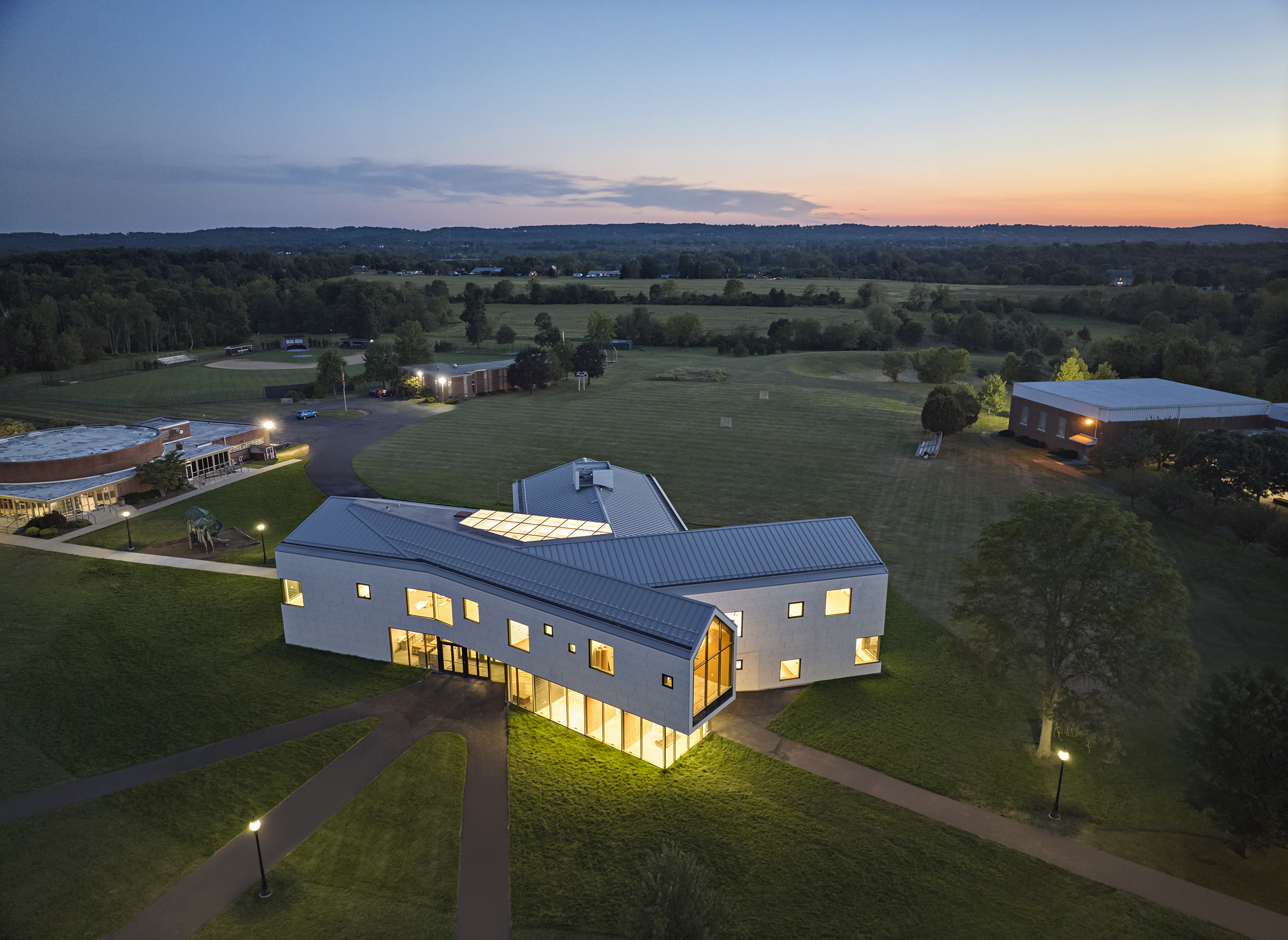 Night time aerial view of Perkiomen School emitting a warm yellow light in the forest of Pennsburg, Pennsylvania