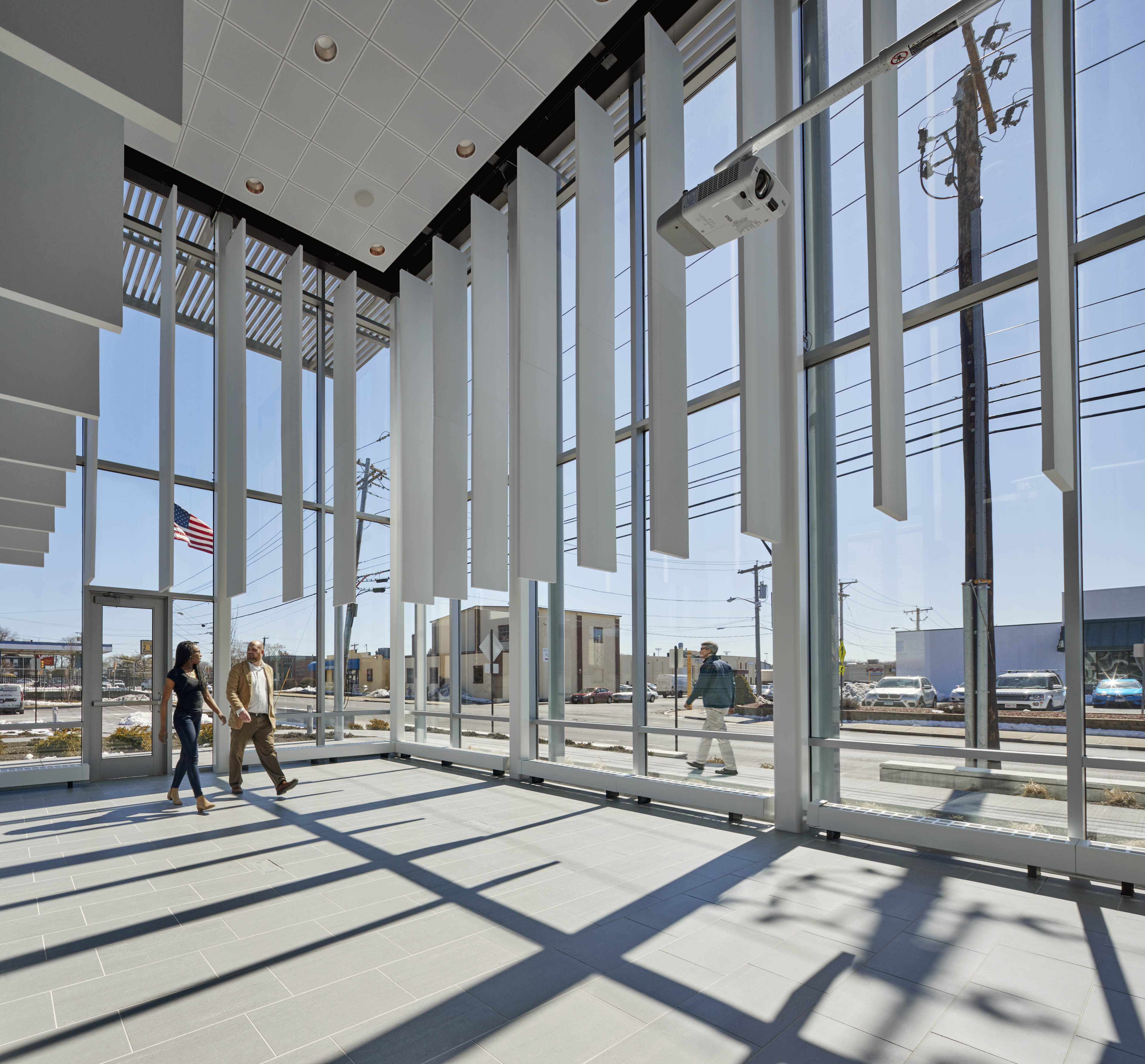 Patrons walking through entrance, both sides of building have floor to ceiling windows with white panels hanging down