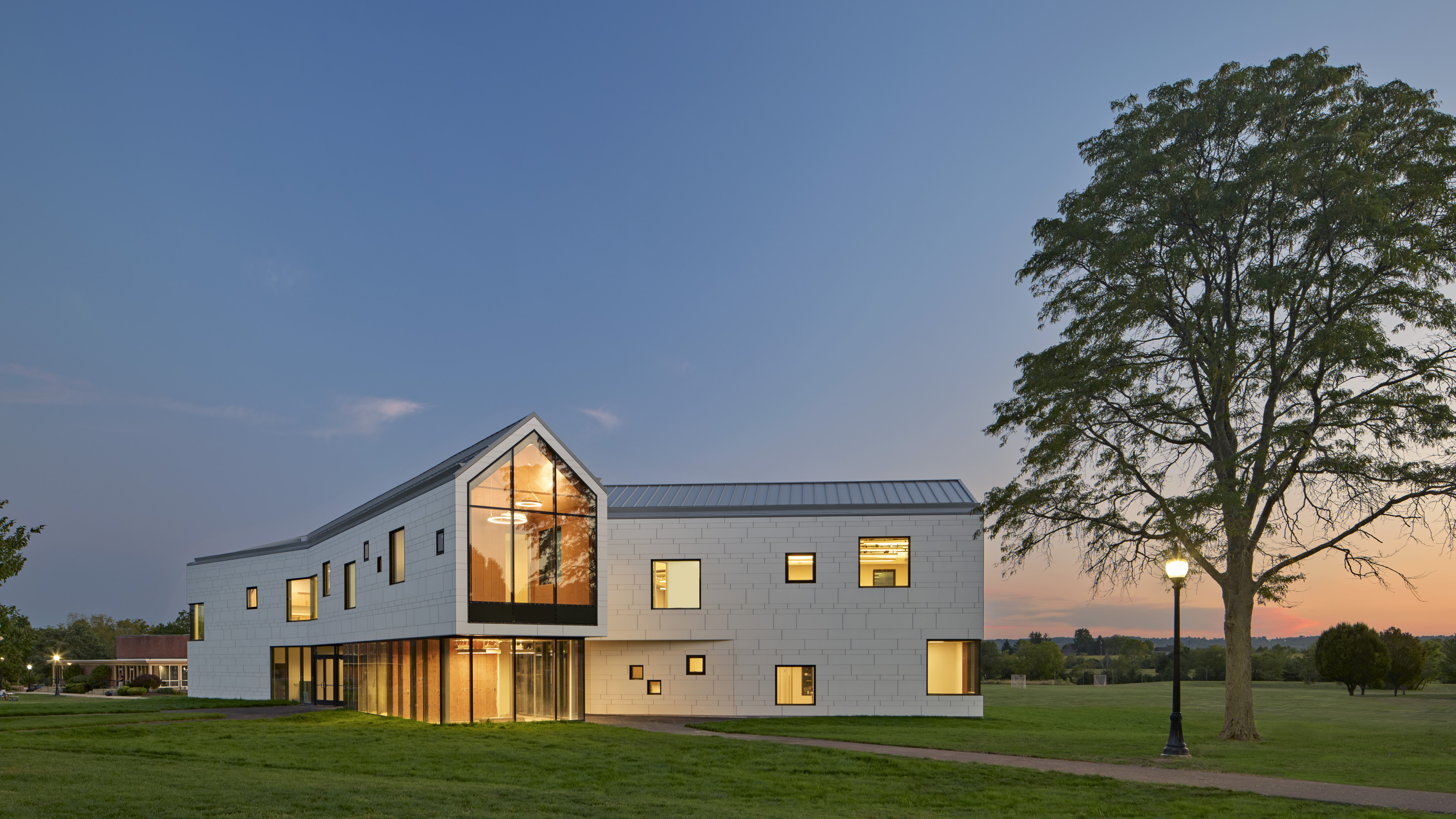 Student center at dusk with tall tree to the right. Yellow amber light emits from large front windows