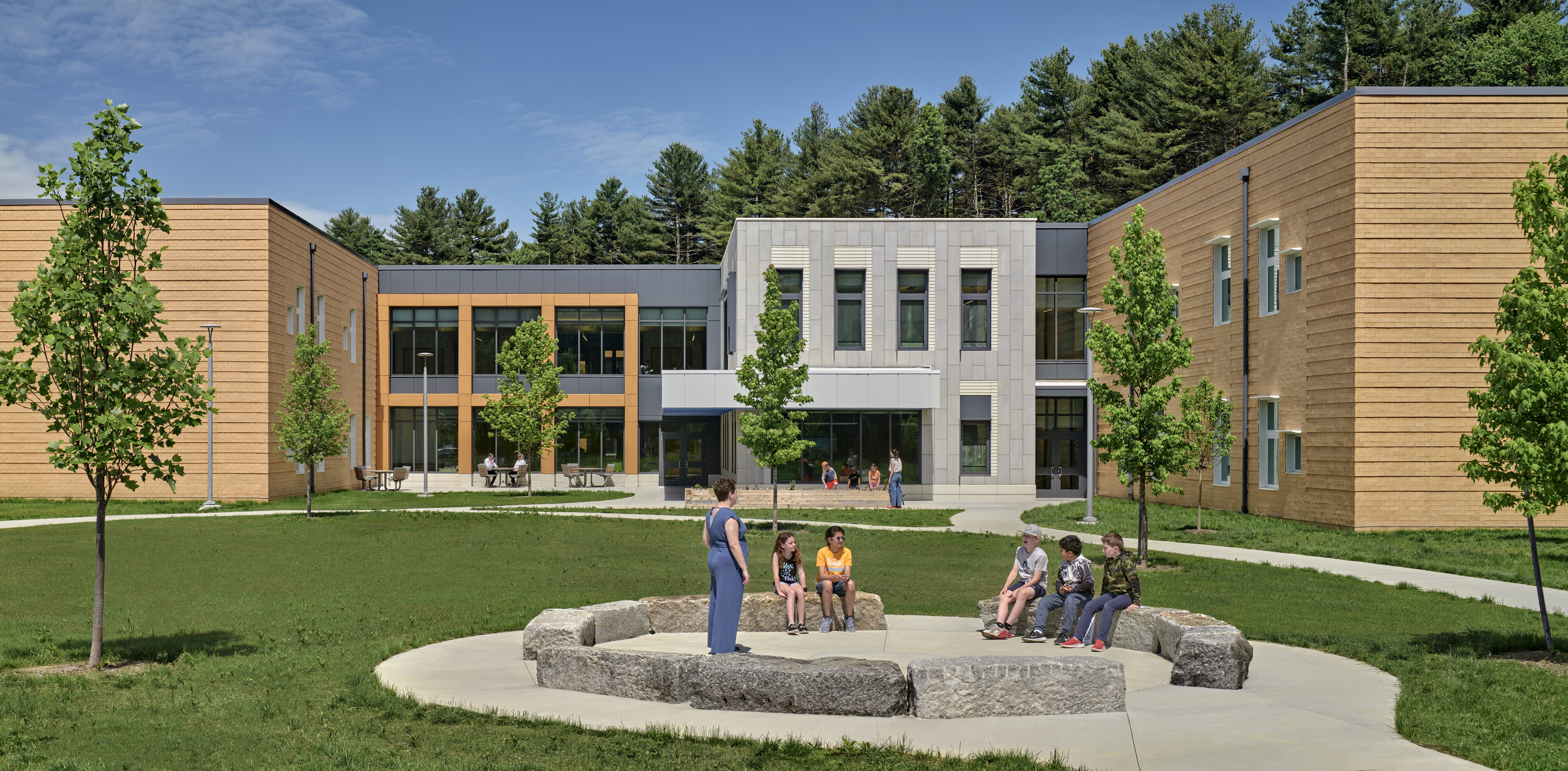 Courtyard of David Mindess School in Ashland, MA, featuring large chunks of stone in a circular formation with students and teachers congregating 