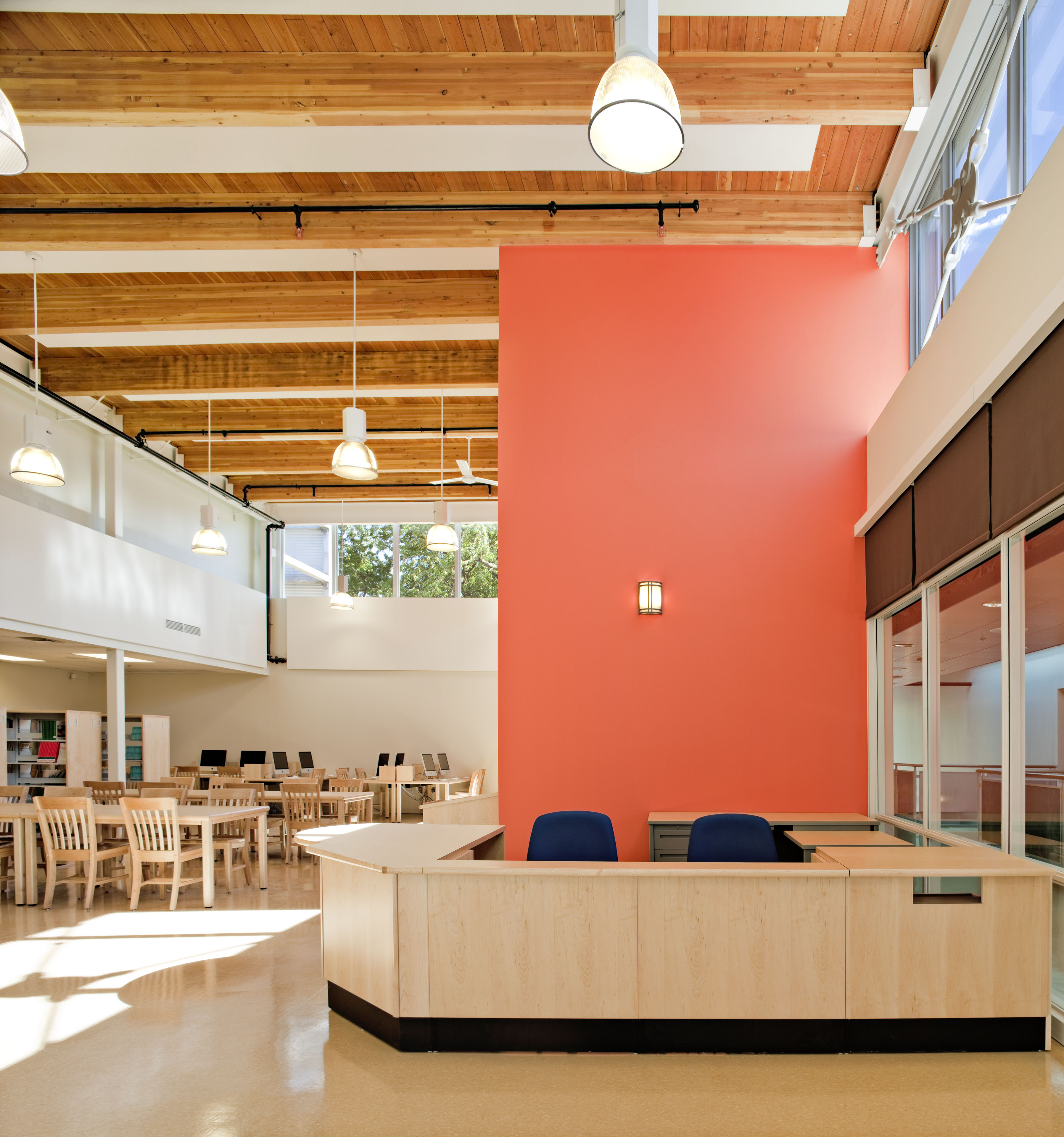 Library with large red wall behind librarian desk and long tables to the left