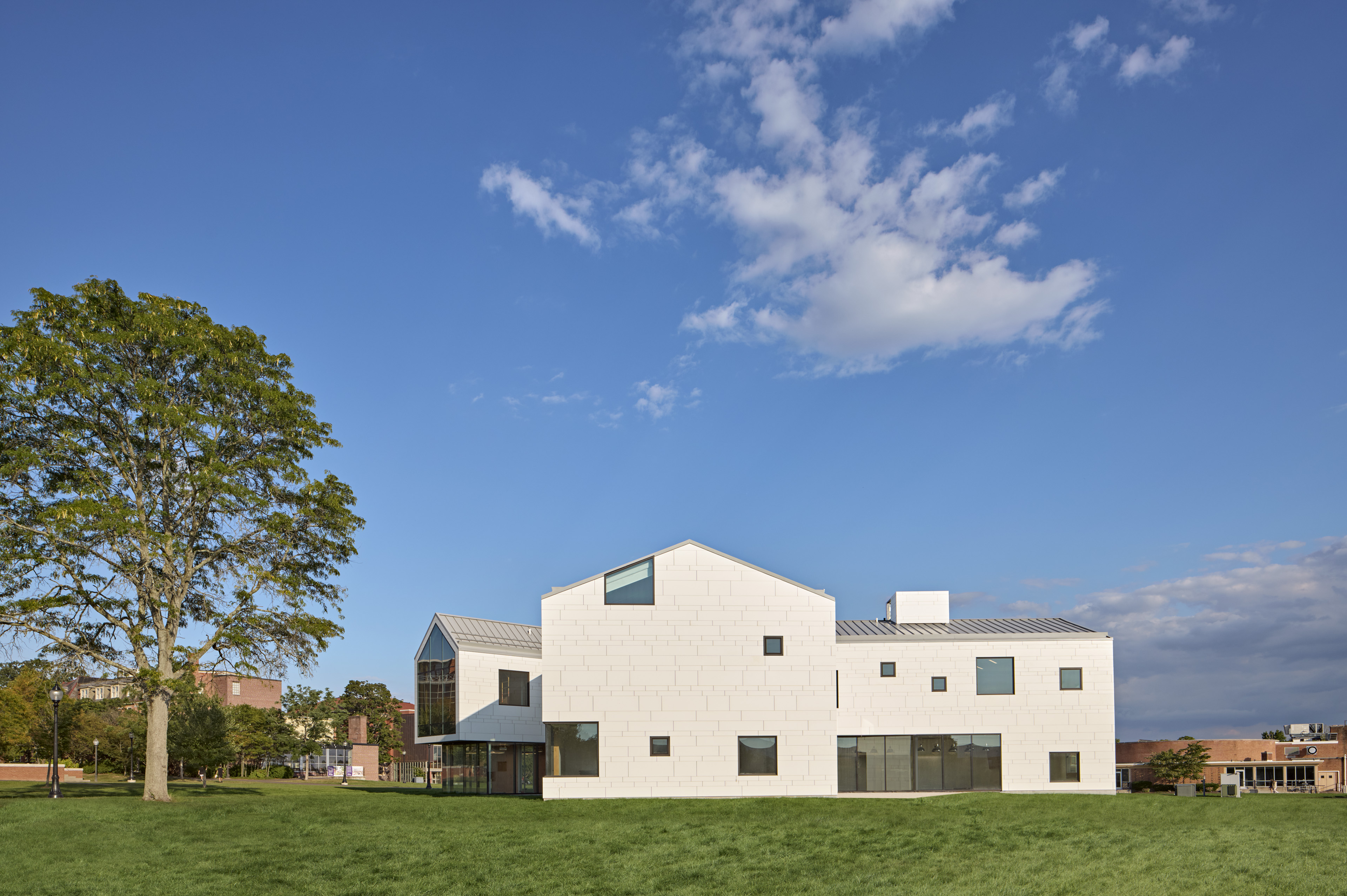 Exterior of student center with barn like structure situated on green grass with blue sky behind. Tall tree to left