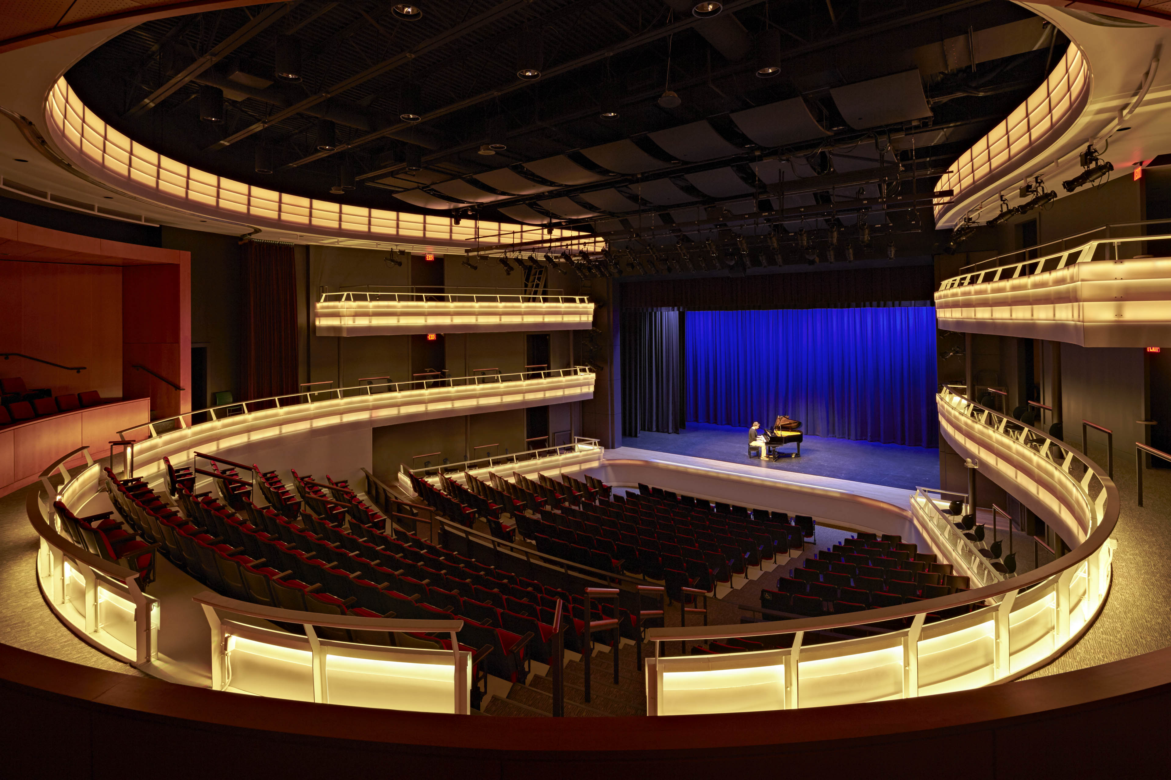 View of theater with lights dimmed. Deep blue light onstage with pianist, yellow lights illuminate balconies