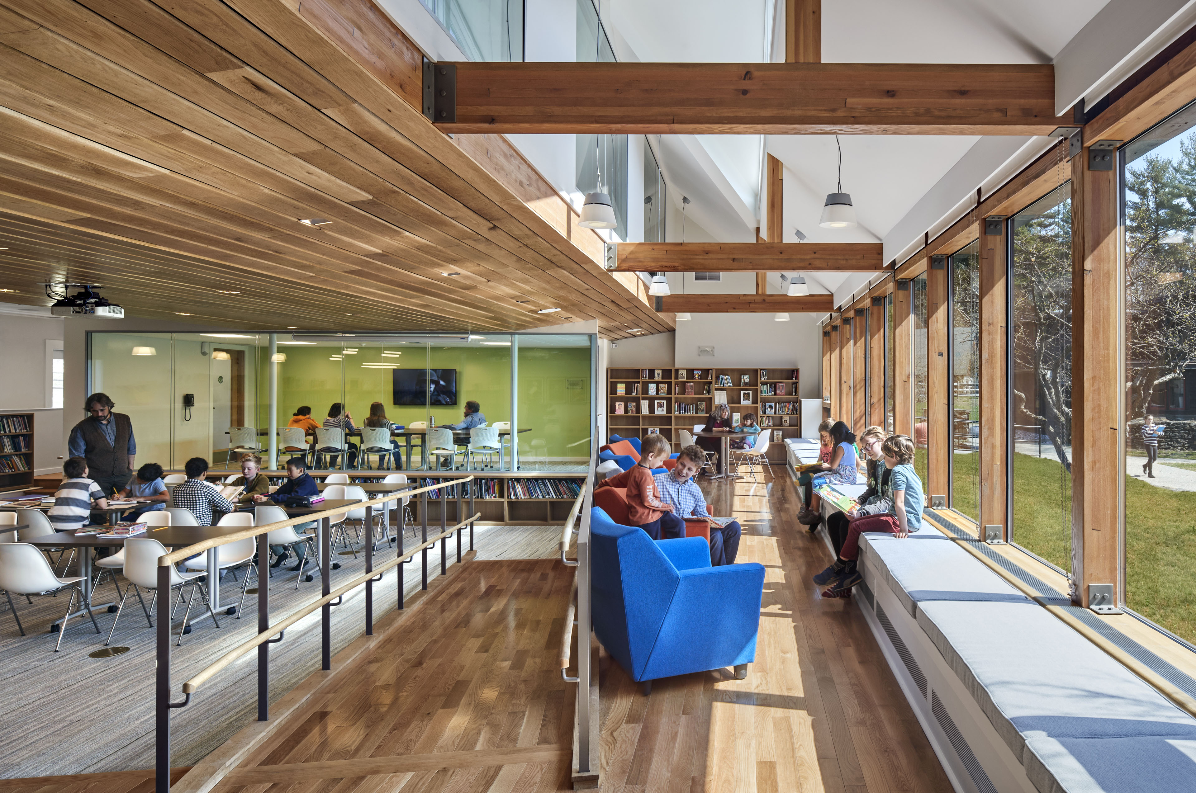 Students reading in classroom with bench lounge seating to the right with windows looking out to lawn, walkway in the middle, and desks to the left