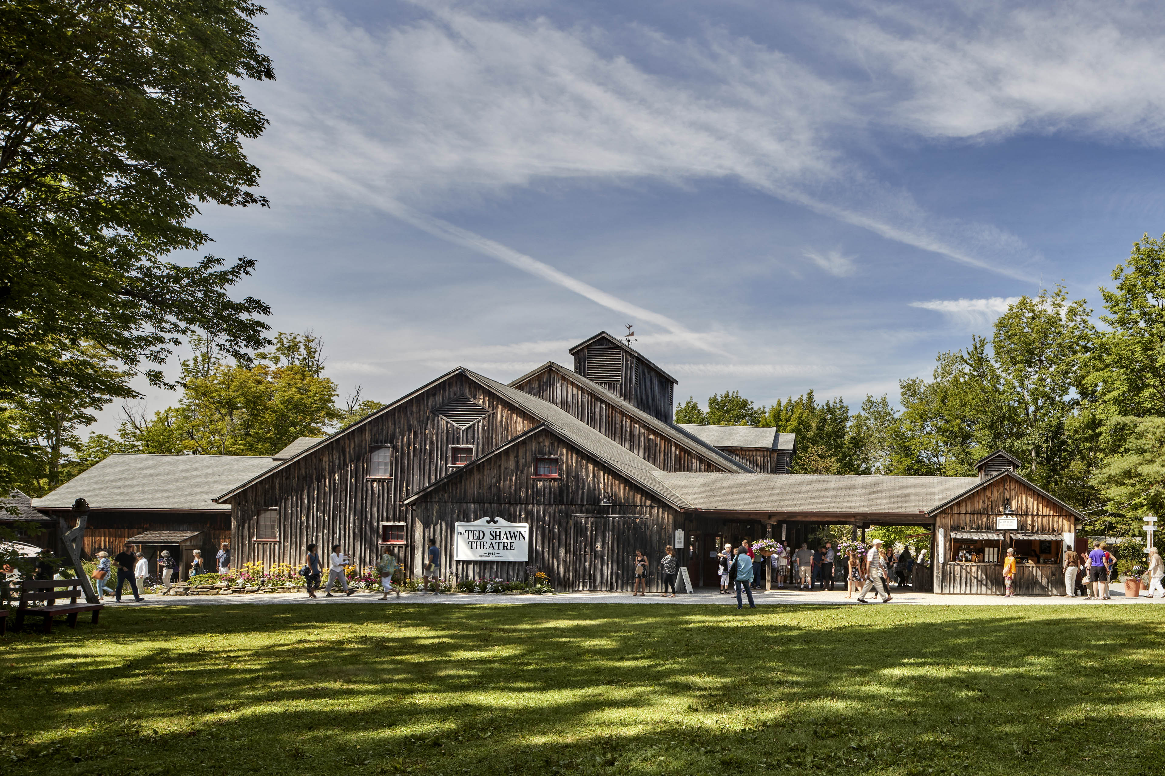Exterior view of building with dark wood siding, grass lawn in front and patrons walking around