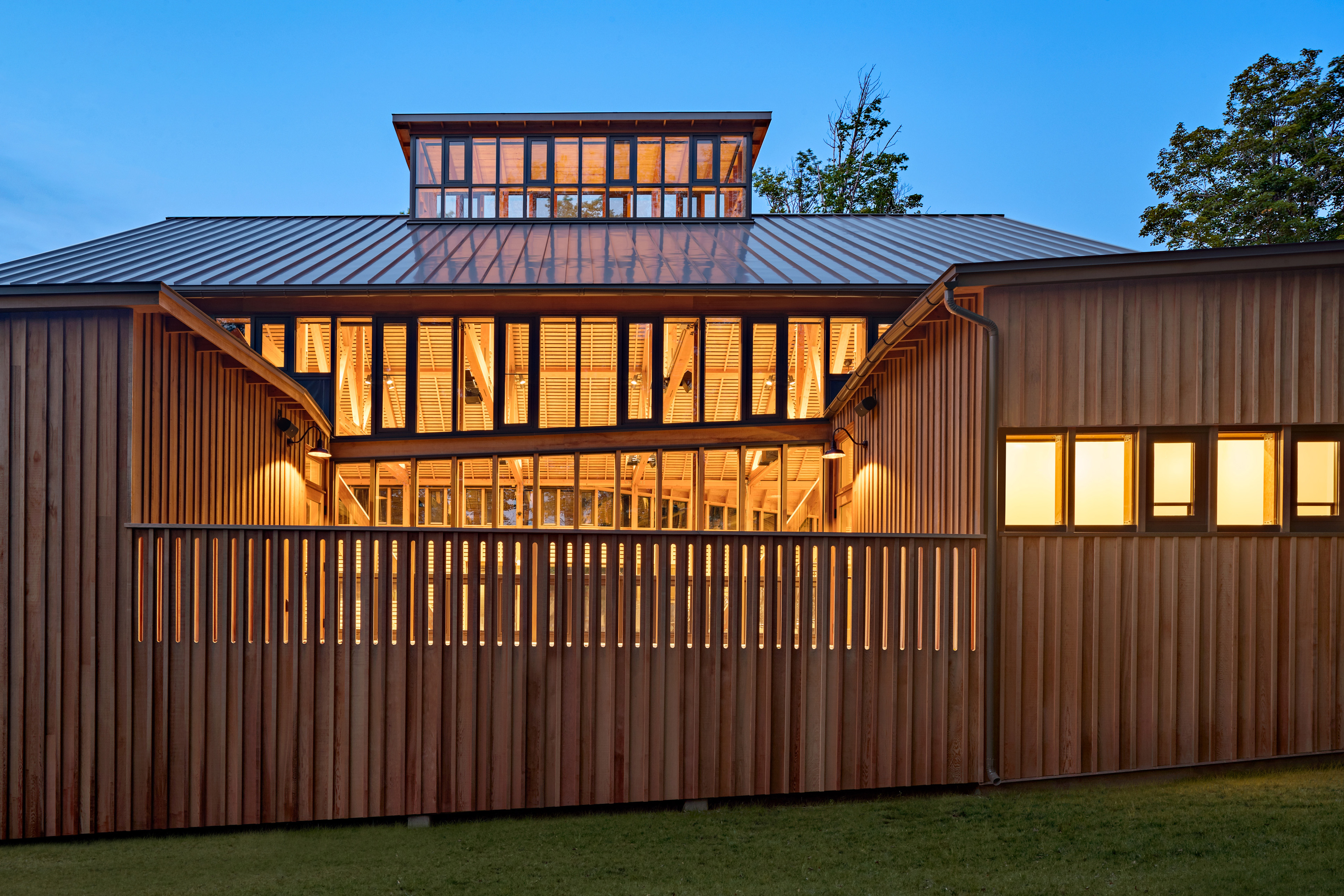 Exterior view of building at night with natural wood siding and green grass in front