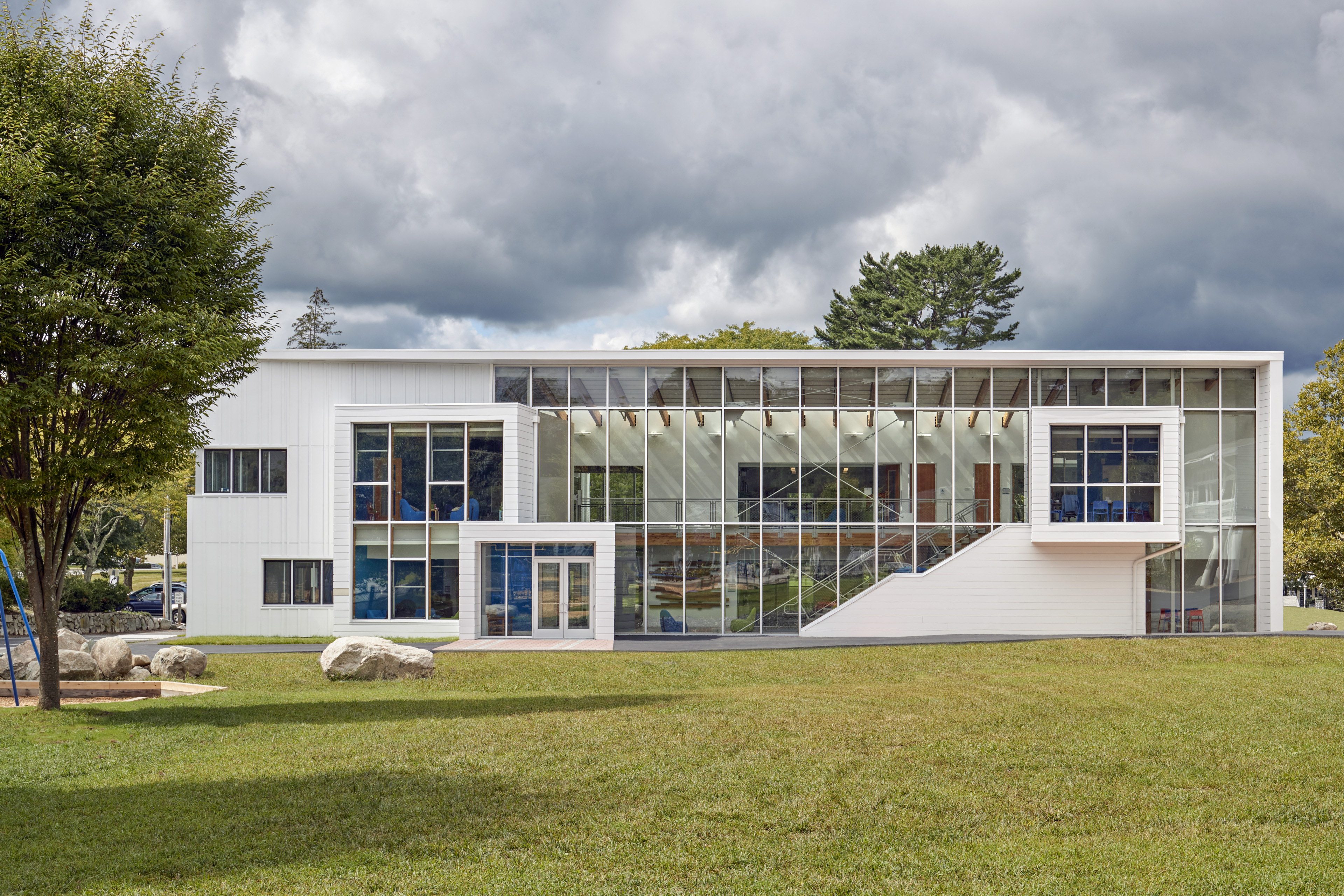 Exterior view of building with white siding and symmetrical windows and tree to the left
