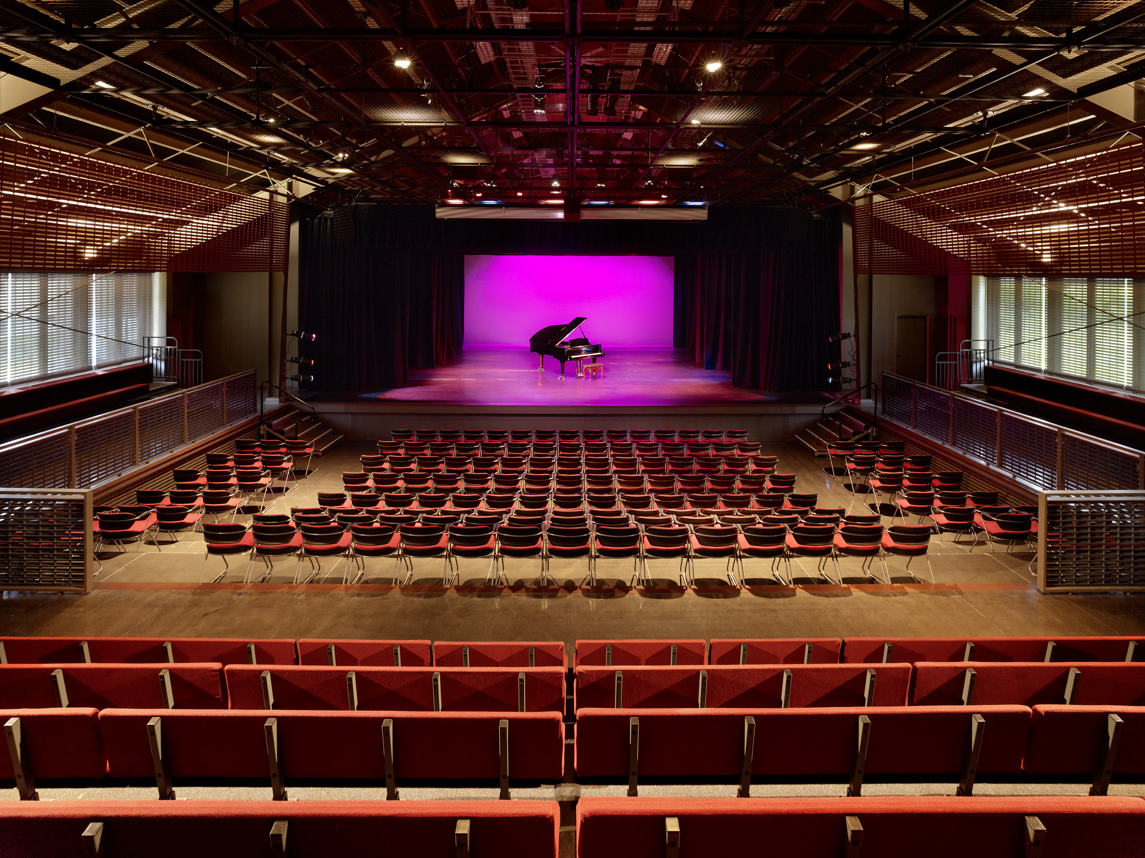 Theater with red seats looking at stage with a grand piano and neon pink light