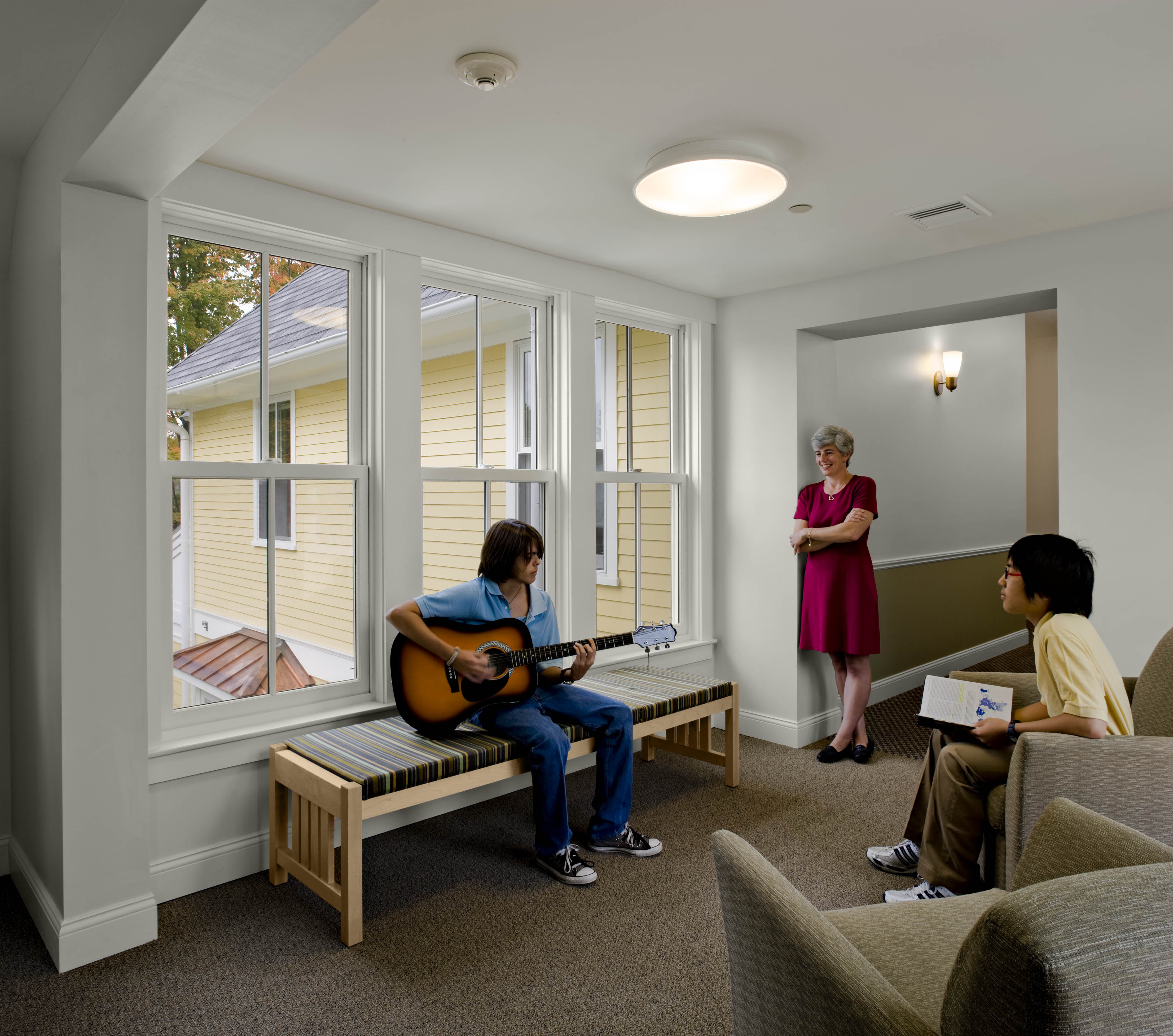 Students playing guitar in lounge area with window to the left