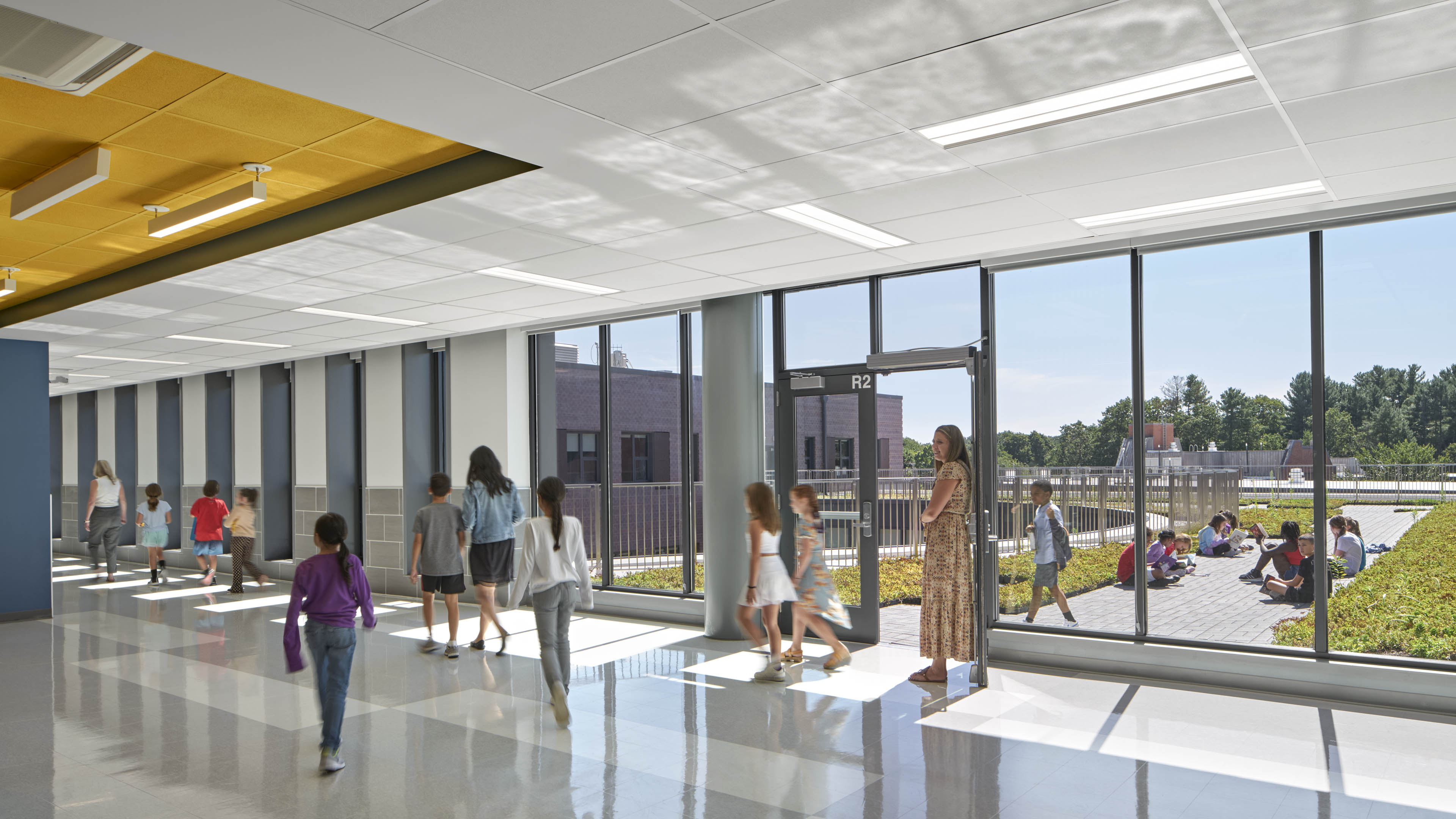 Students walking through interior corridor with floor to ceiling windows looking out to walking area