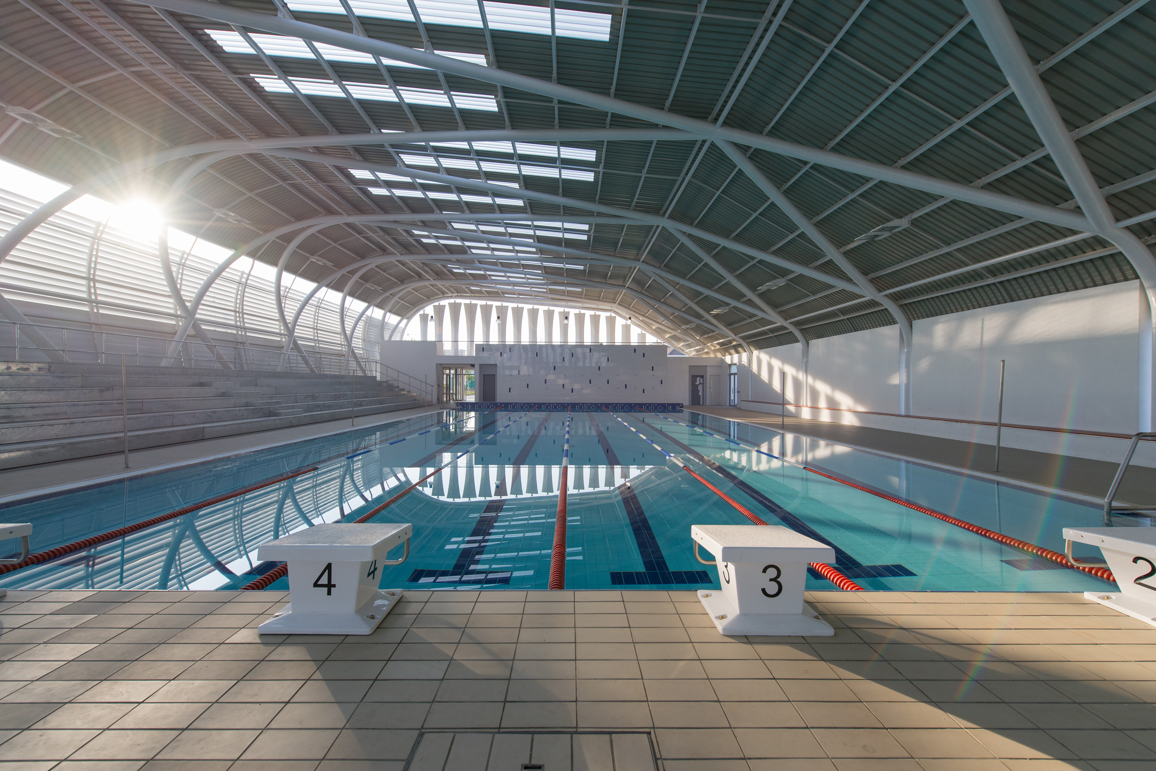 Indoor pool with lane lines and ample sunlight, starting blocks with numbers in front