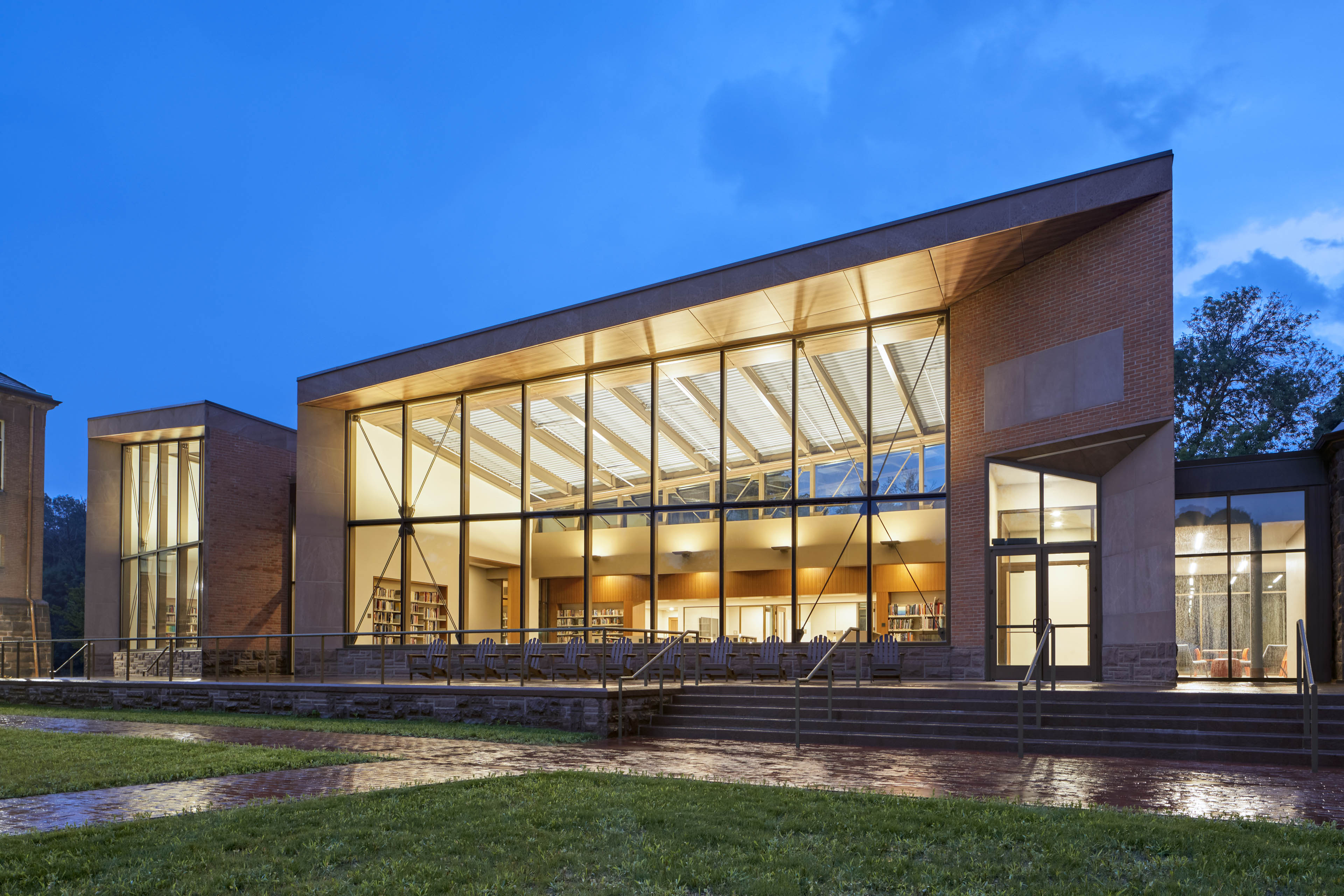 View of exterior of building at night with yellow light glowing out. Walkway in front with grass on both sides