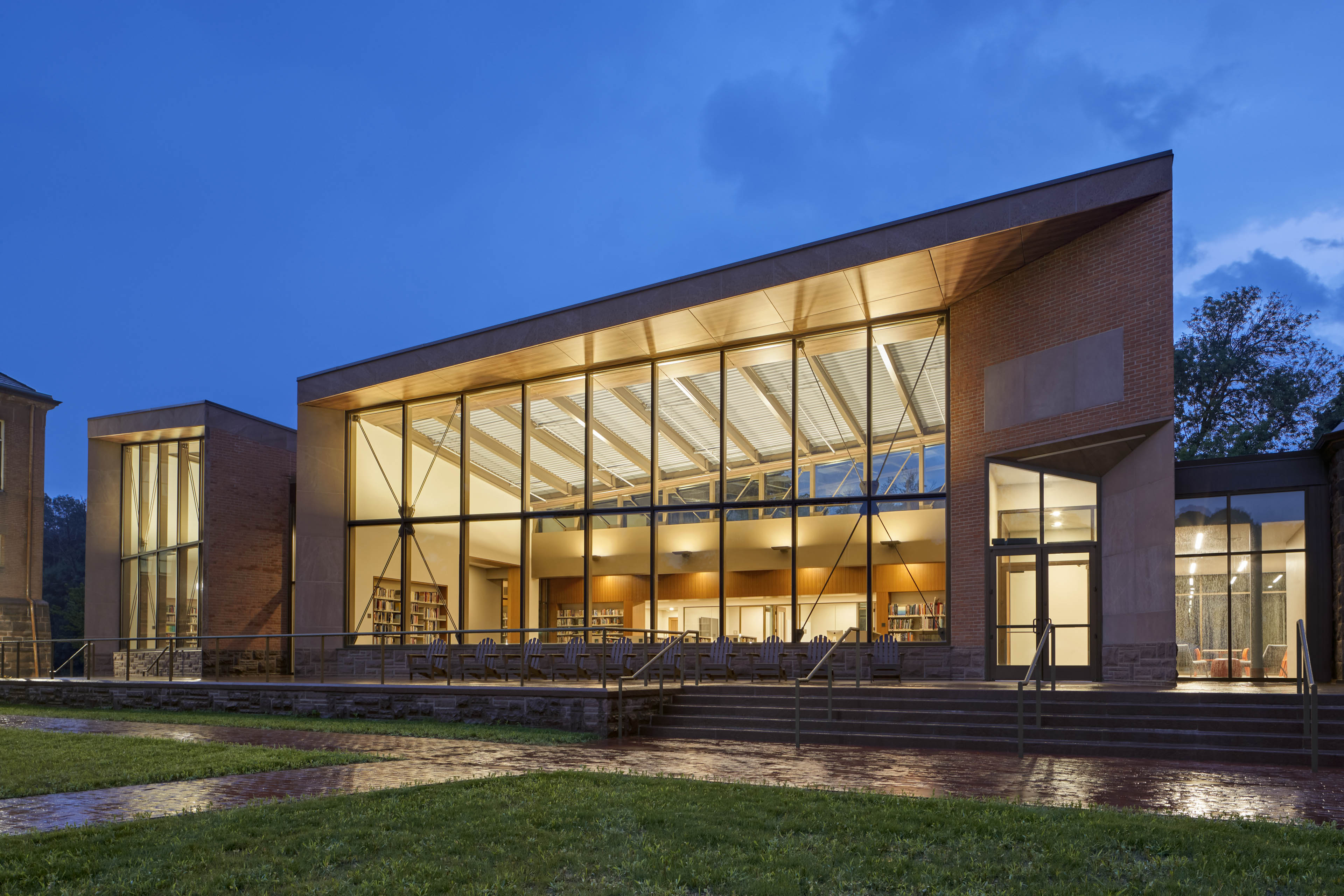 View of exterior of building at night with yellow light glowing out. Walkway in front with grass on both sides
