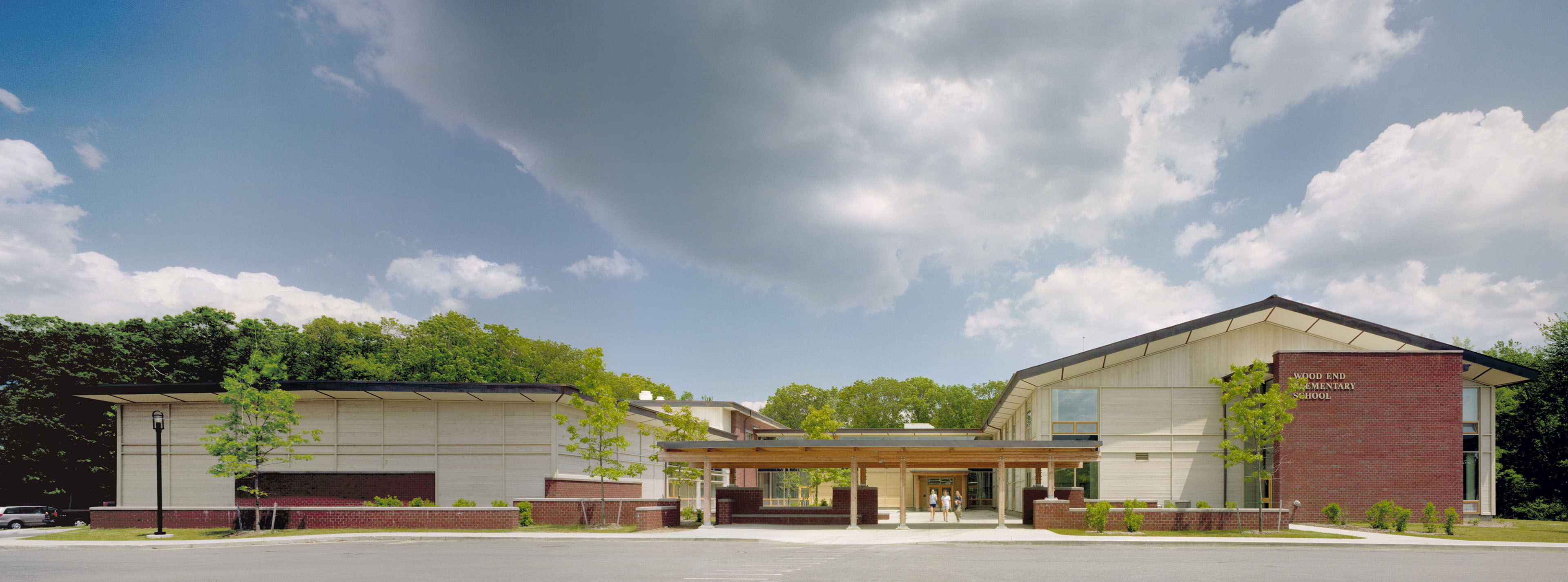 2 buildings connected by pergola, bright green trees extend from background and blue sky with large white clouds above