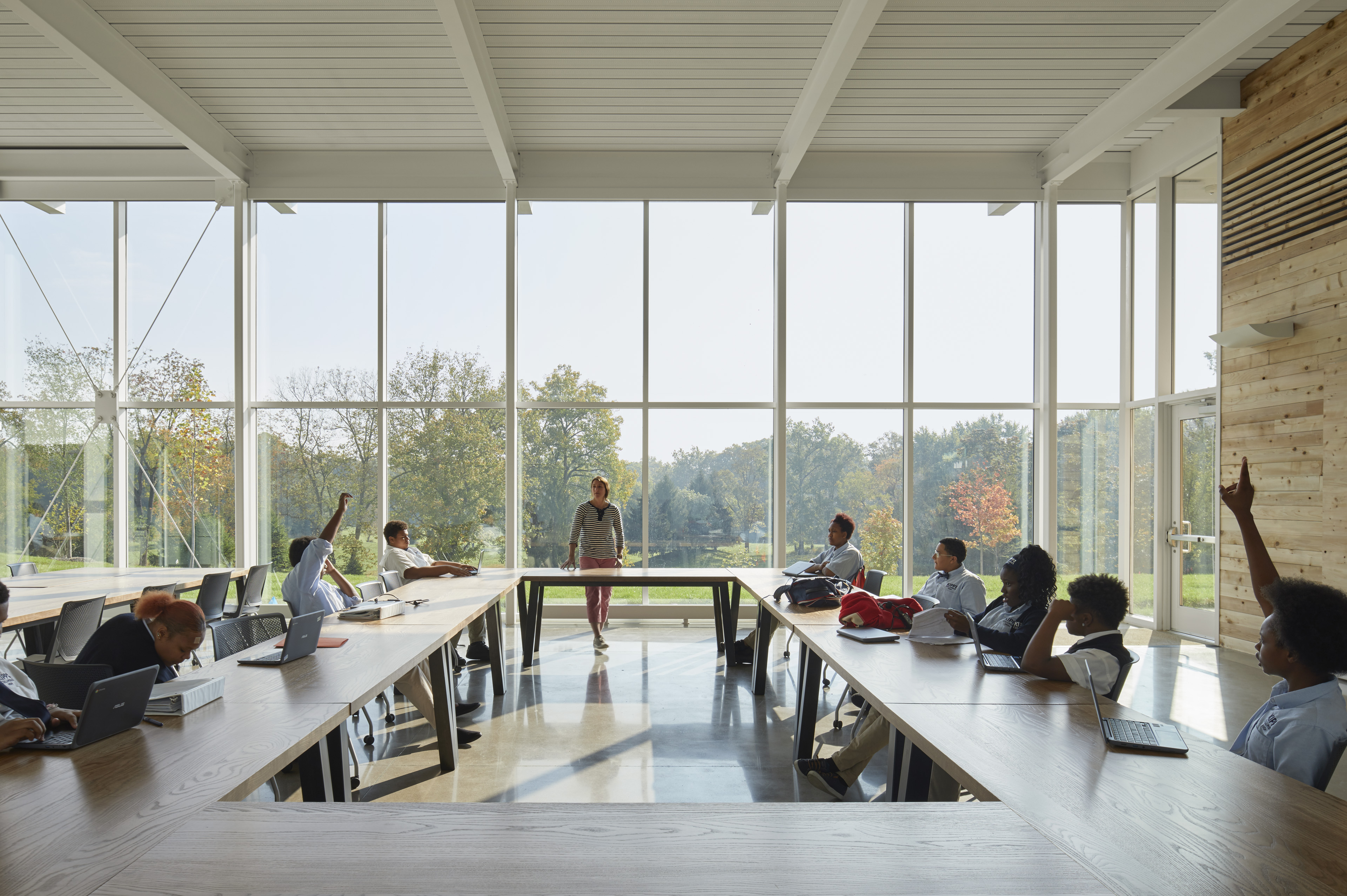 Students sat around tables in large square formation with large windows looking out to field behind