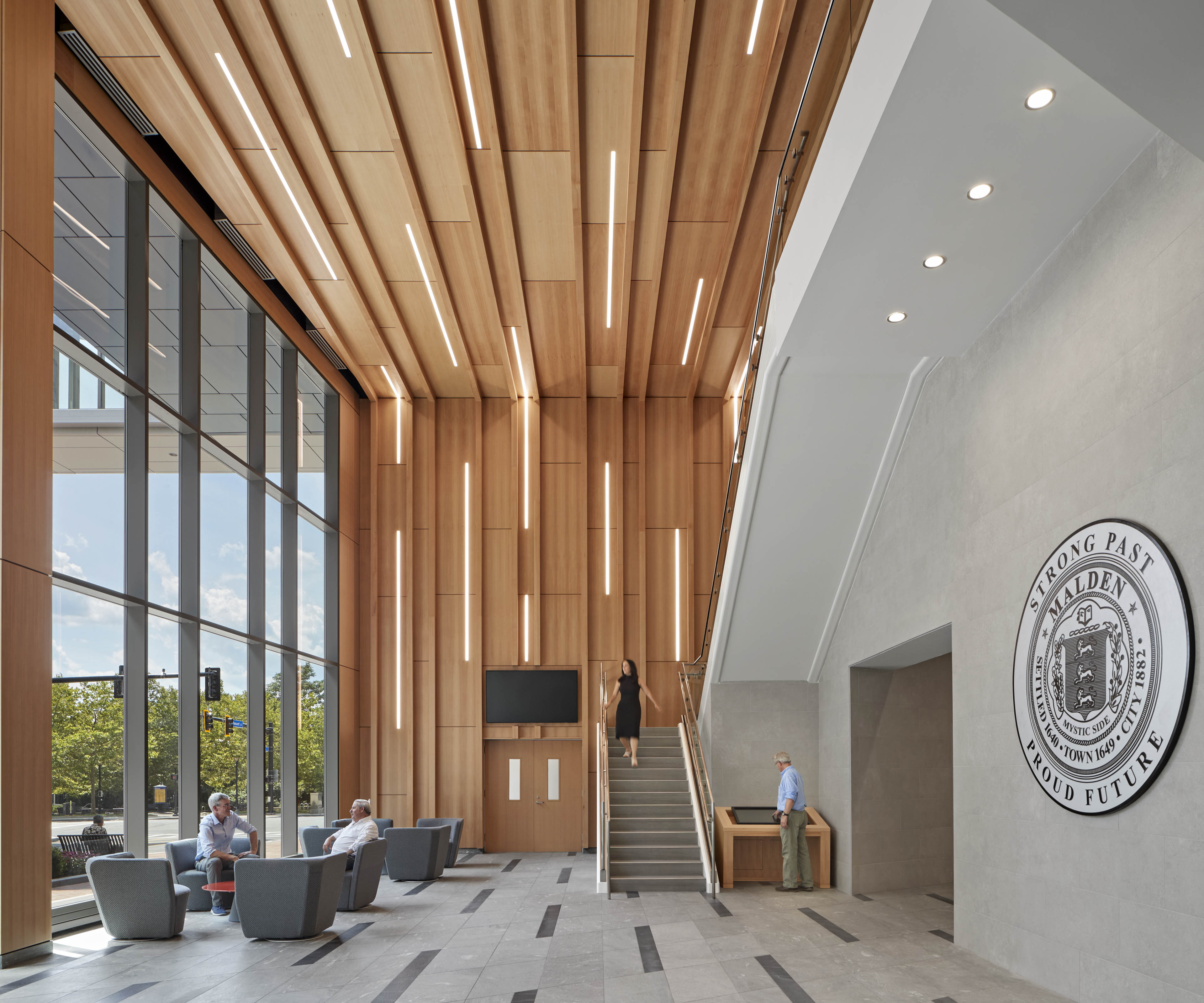 View of lobby with light wood covering back wall, stairs in back and town crest to on wall to the right