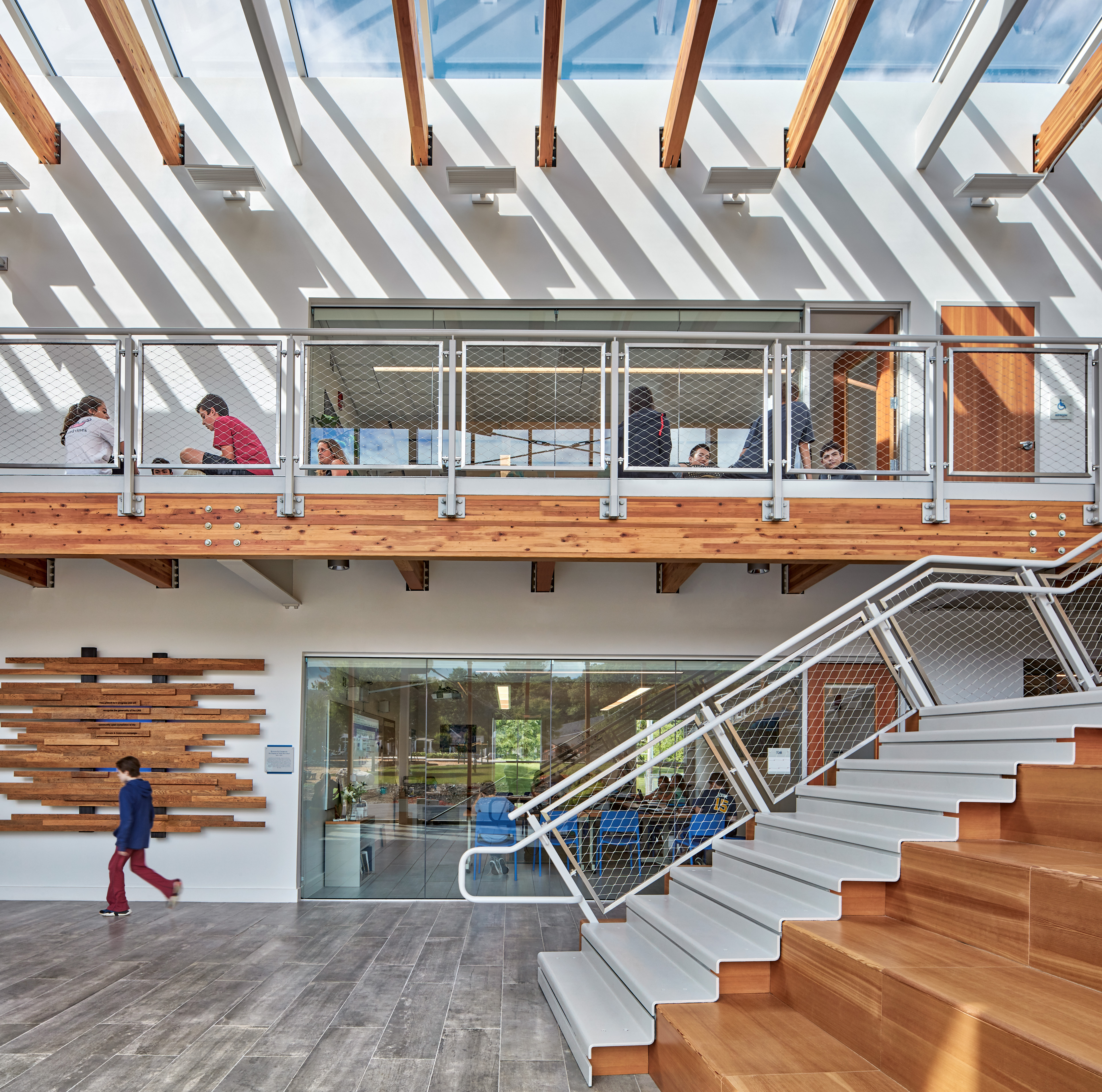 Interior corridor with stairs to the right and second floor walkway above, windows on ceiling with natural light coming in