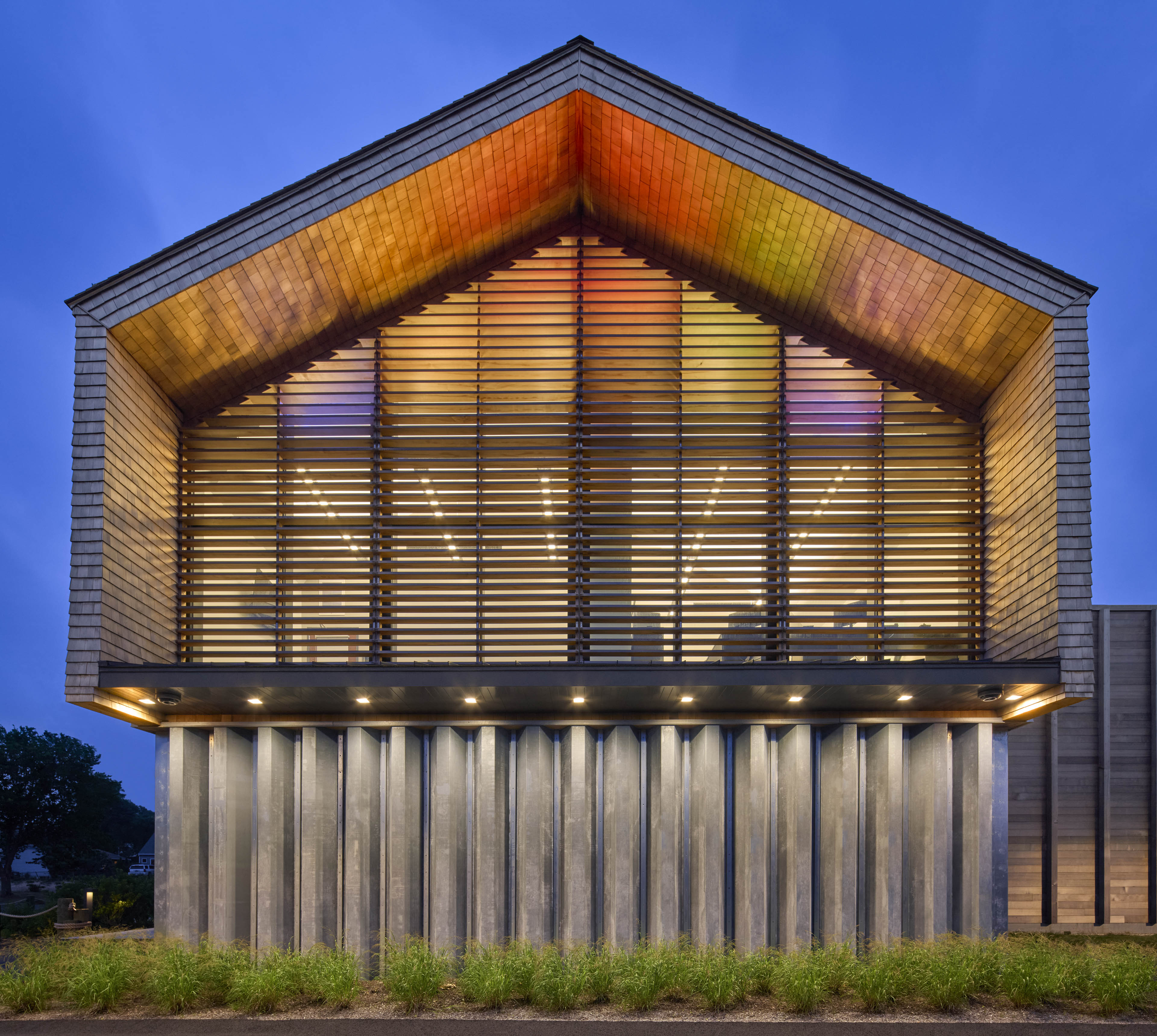 Exterior of building at night with colored light filtering though slats on the second floor 