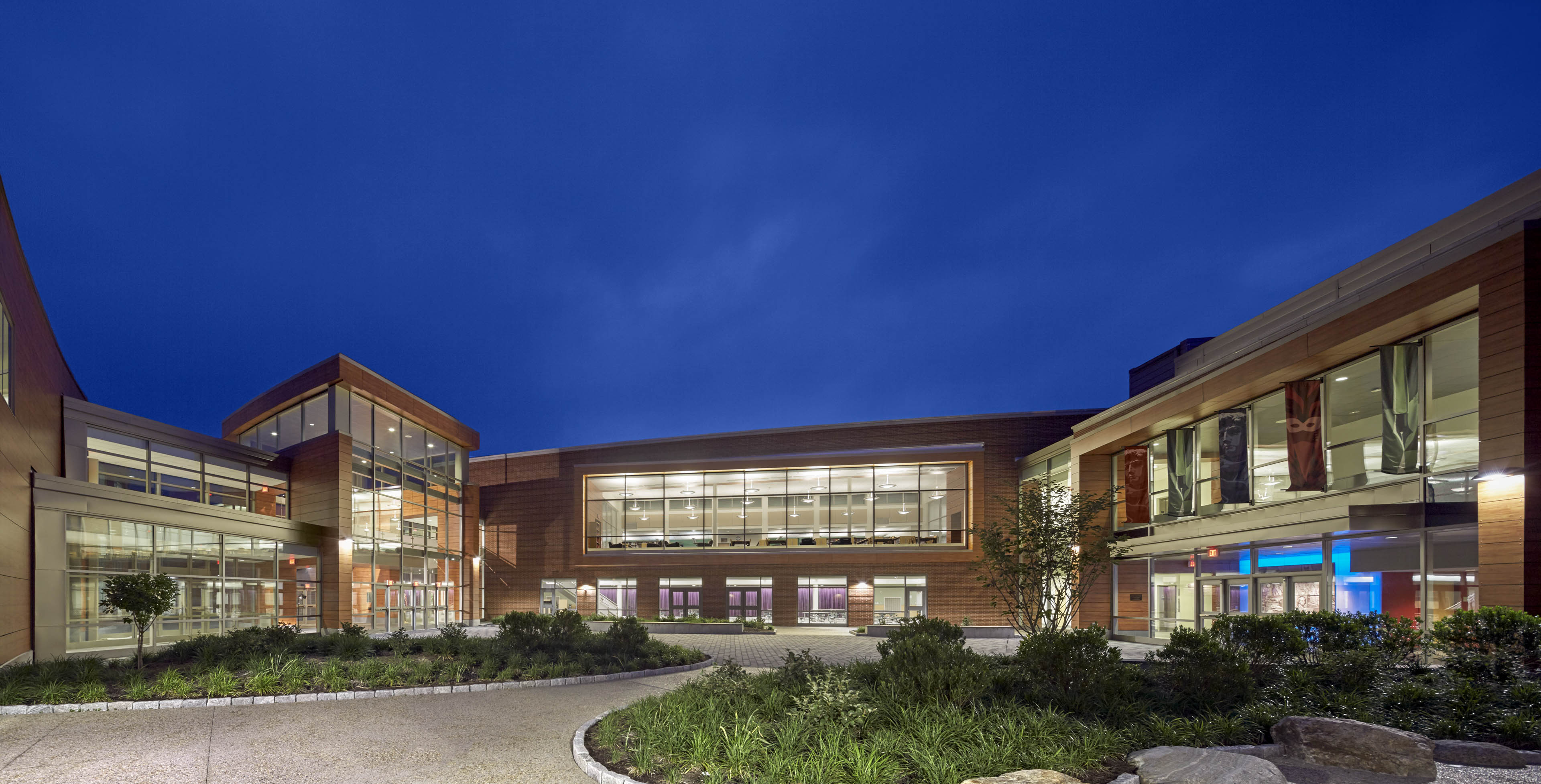 Wide angle view of entrance of school at night with deep blue sky behind and greenery in front