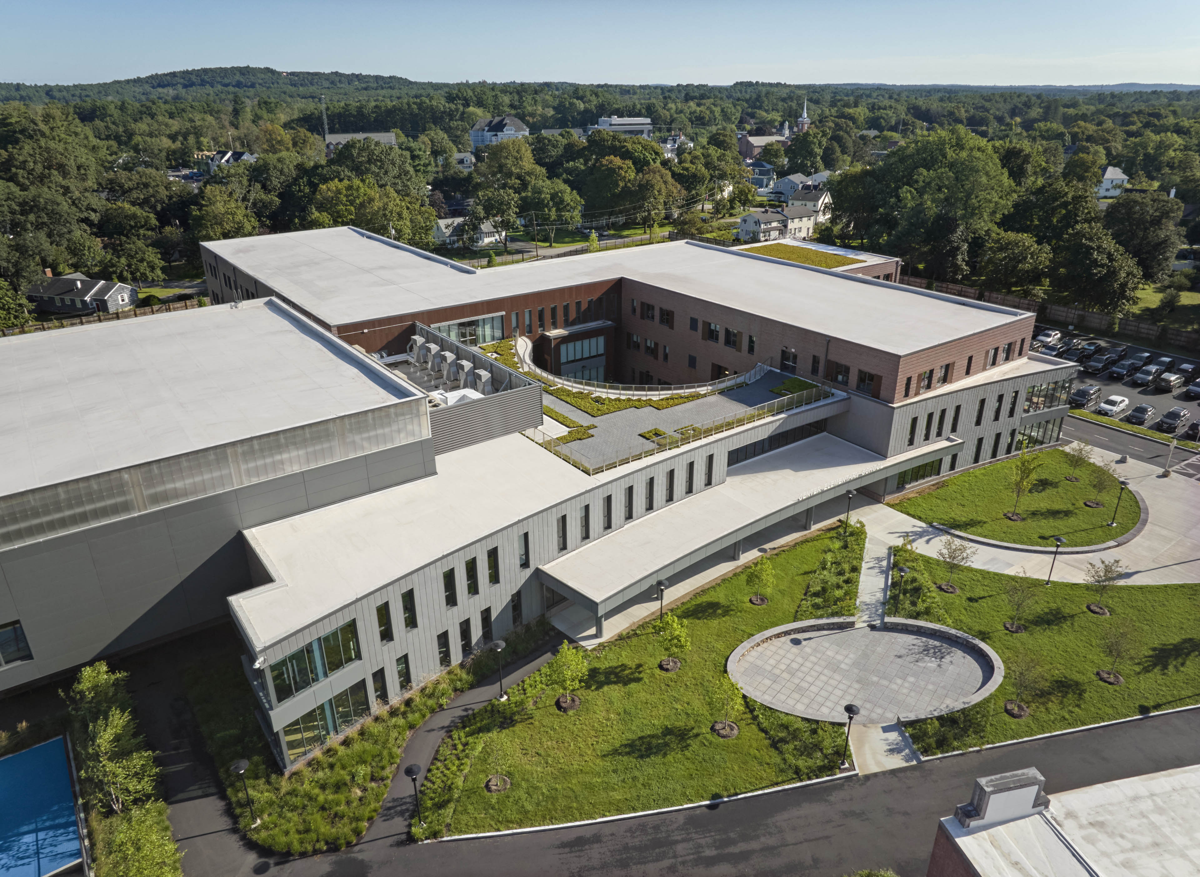 Aerial overview of school with ample tree coverage behind and grass in front
