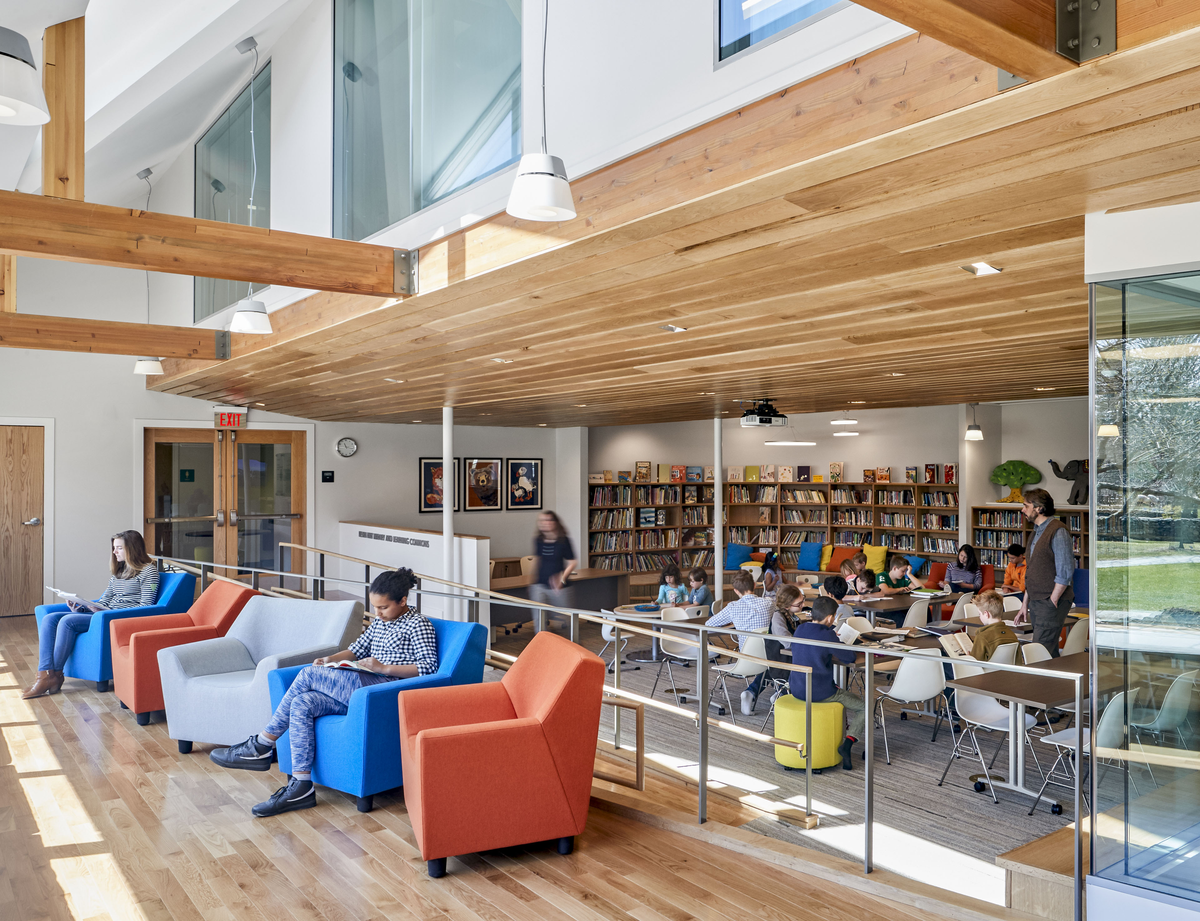 Students reading in classroom with bench lounge seating to the left, walkway in the middle, and desks to the right