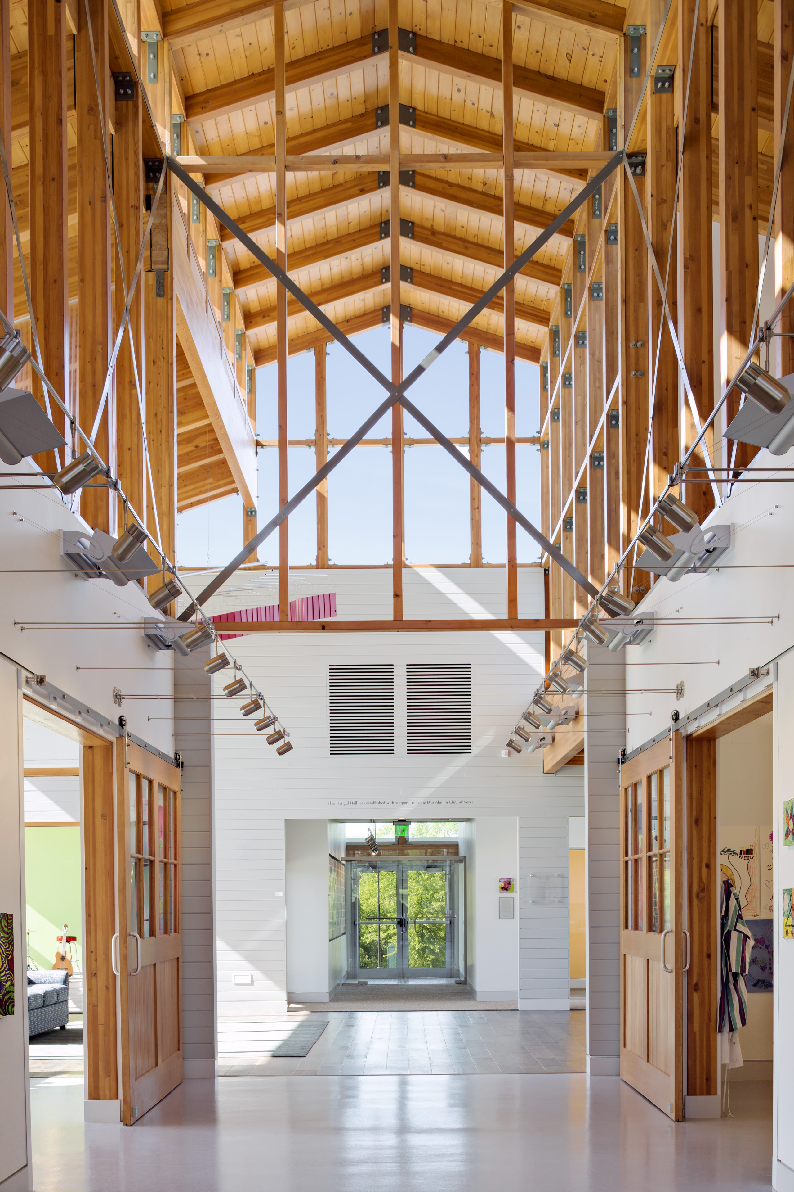 Interior corridor looking at second floor ceiling, long poles in x formation with natural wood beams around 