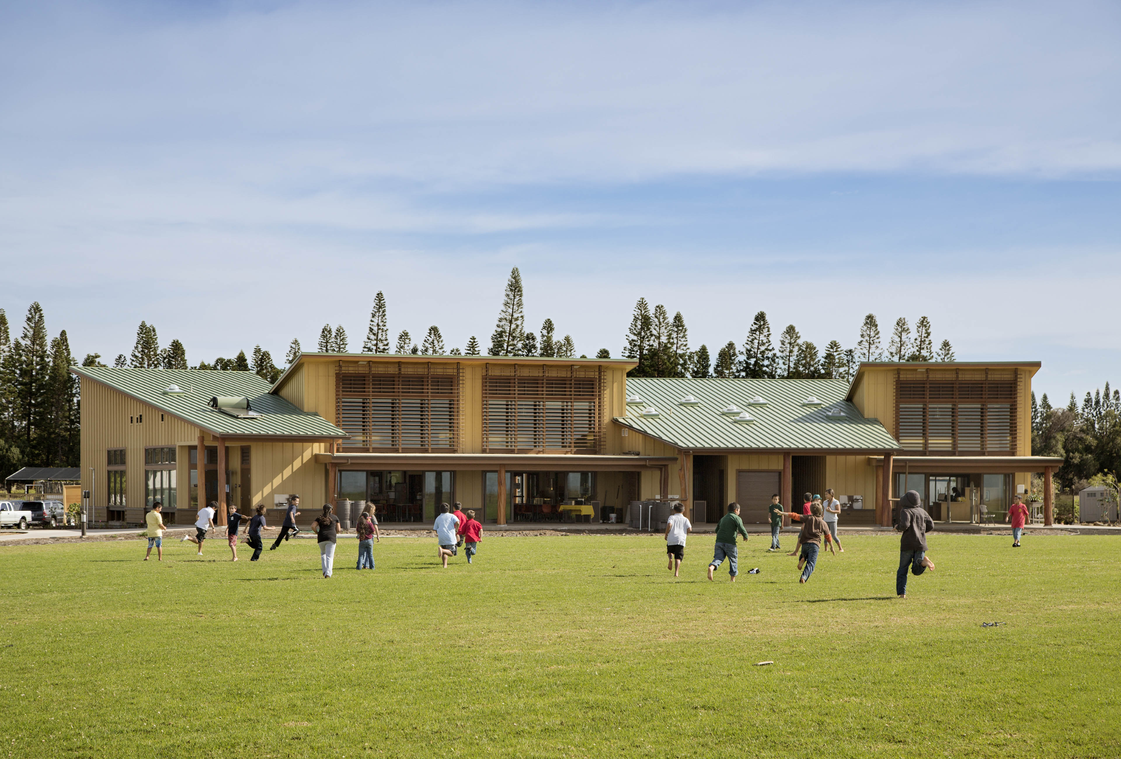 View of exterior from grass with students running up to building. Trees peeping out from behind and blue skies