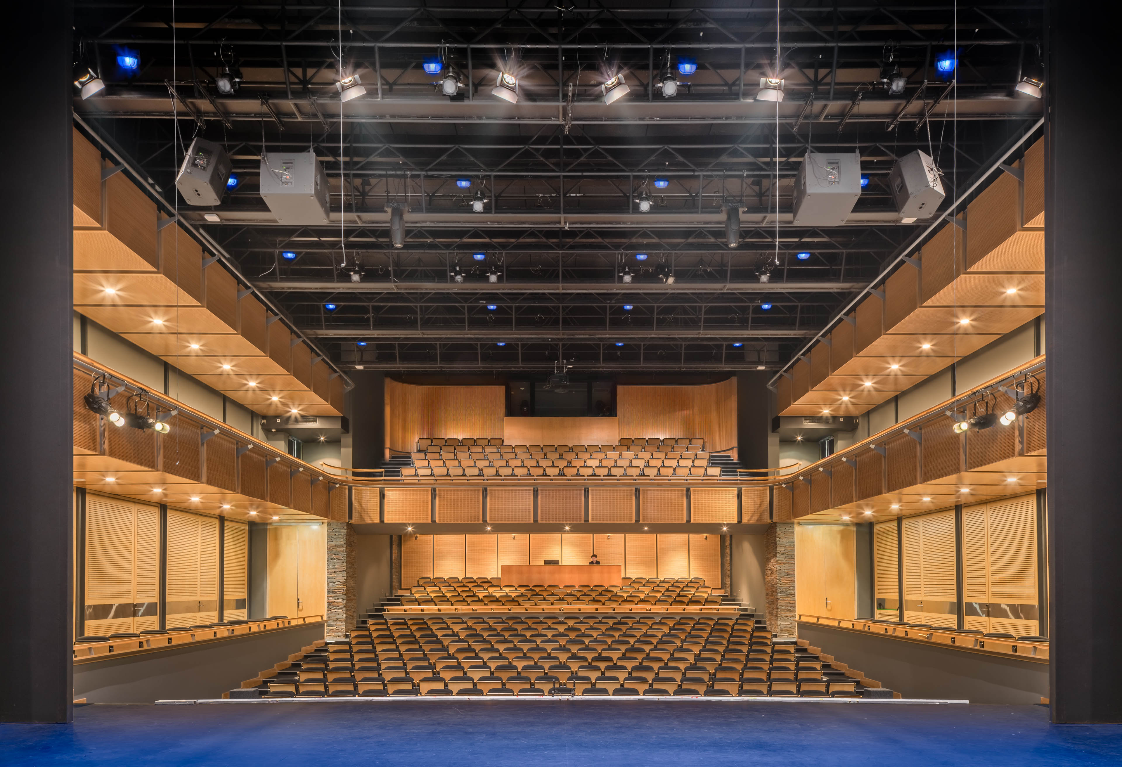 View of theater from back of stage, empty seats with lights on and tech controller on second floor