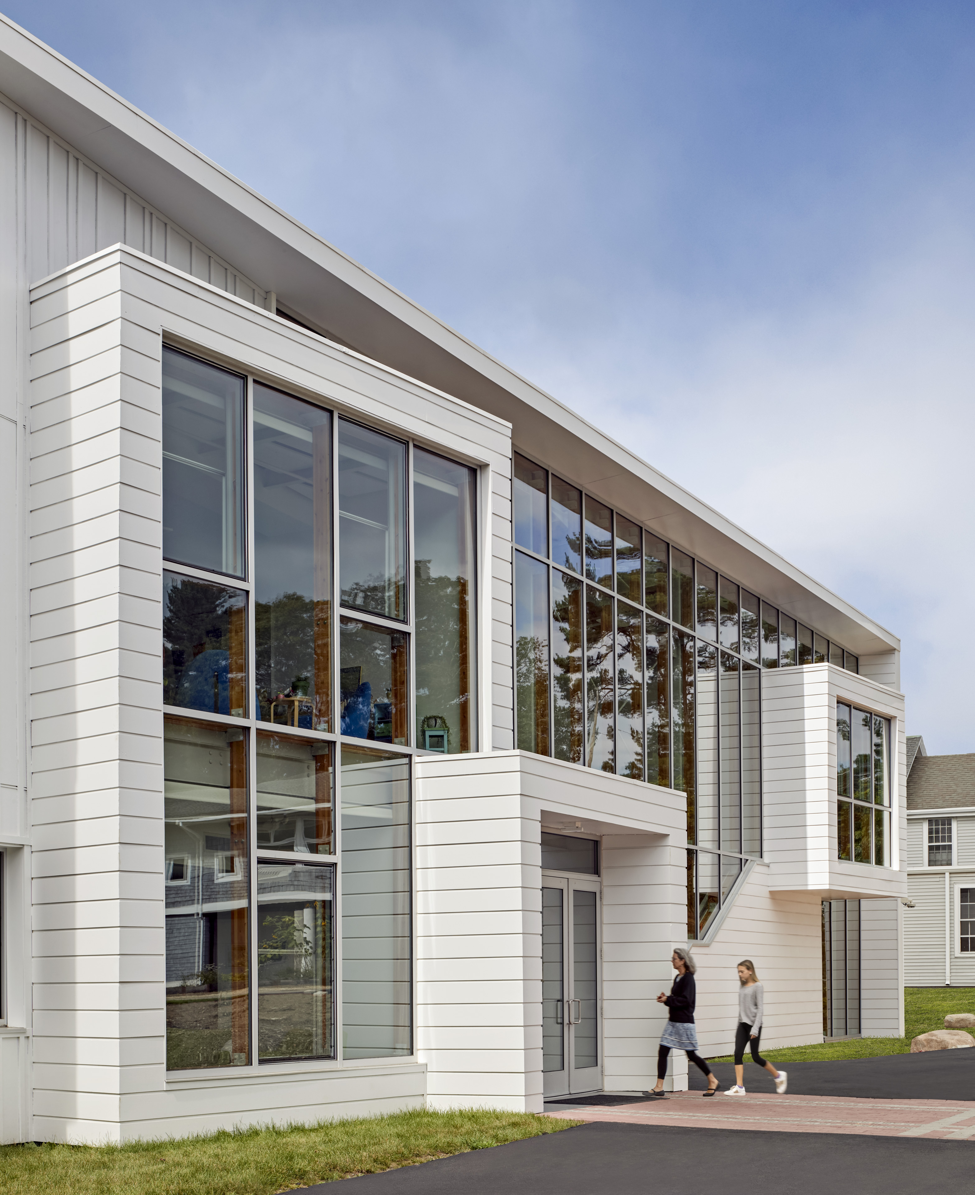 Back view of building with large windows and people walking in with blue sky behind