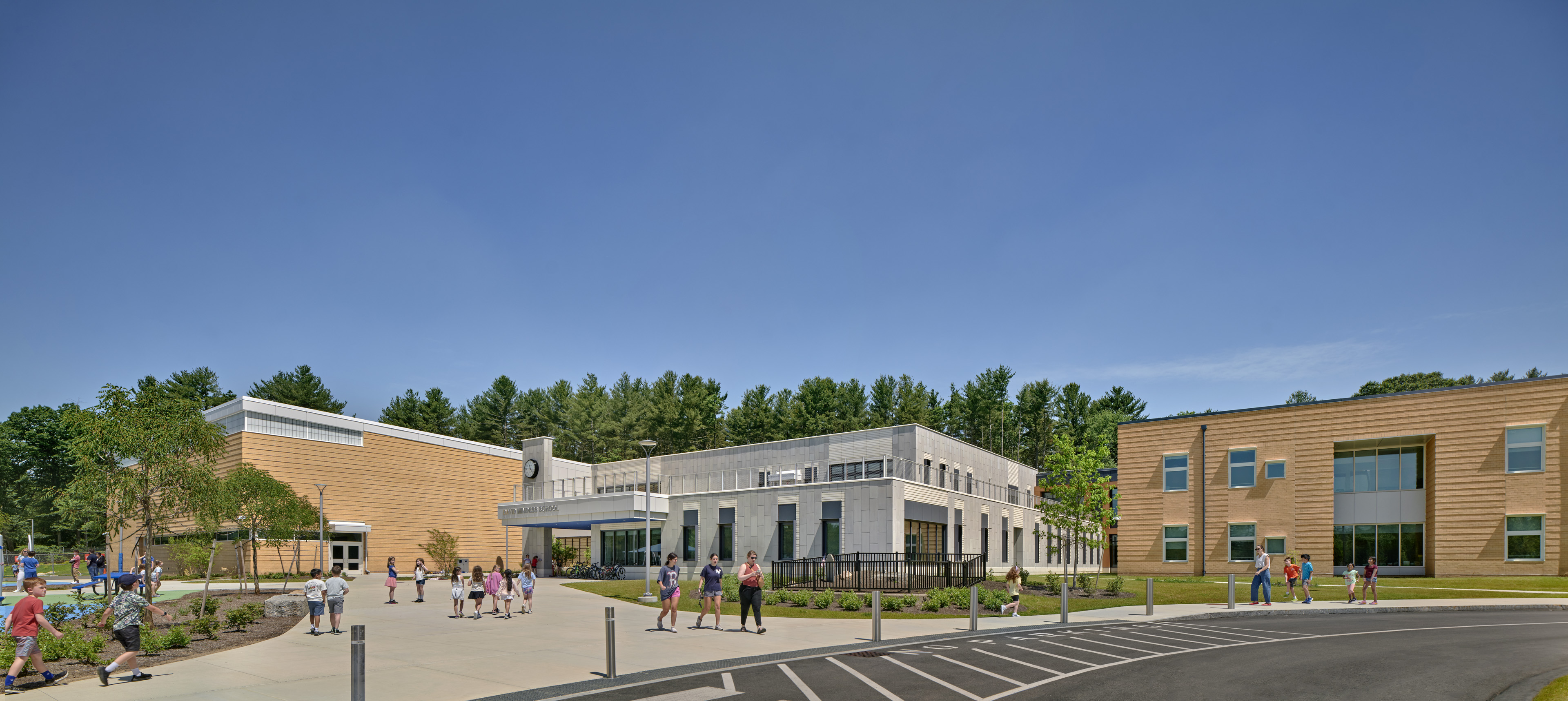 Students walking around school near drop off lane, school in background with trees behind and blue sky